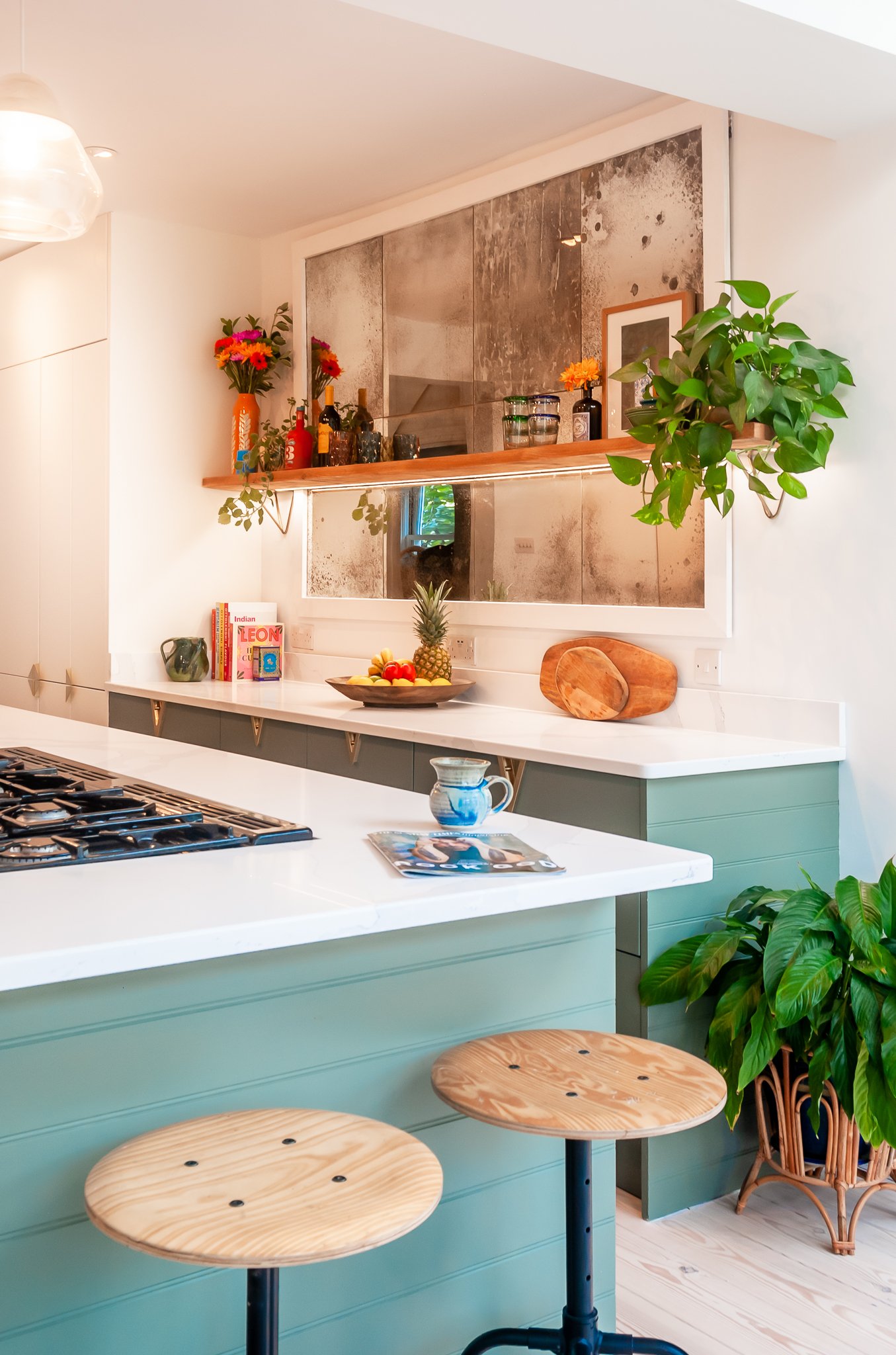 Kitchen in Brockley with peninsula seating, hand-antiqued mirror splashback, open shelving, plants and warm personal styling details.