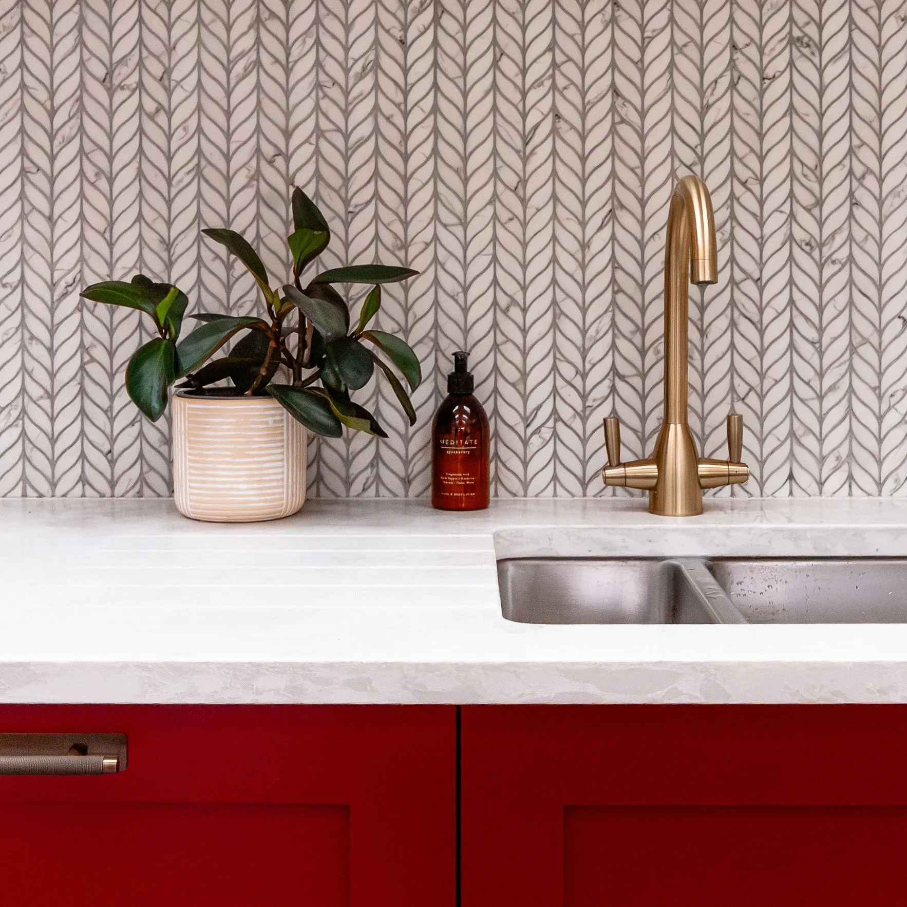 Detail of the red kitchen cabinetry in Forest Hill, with brass tap, quartz worktop and leaf mosaic splashback tiles