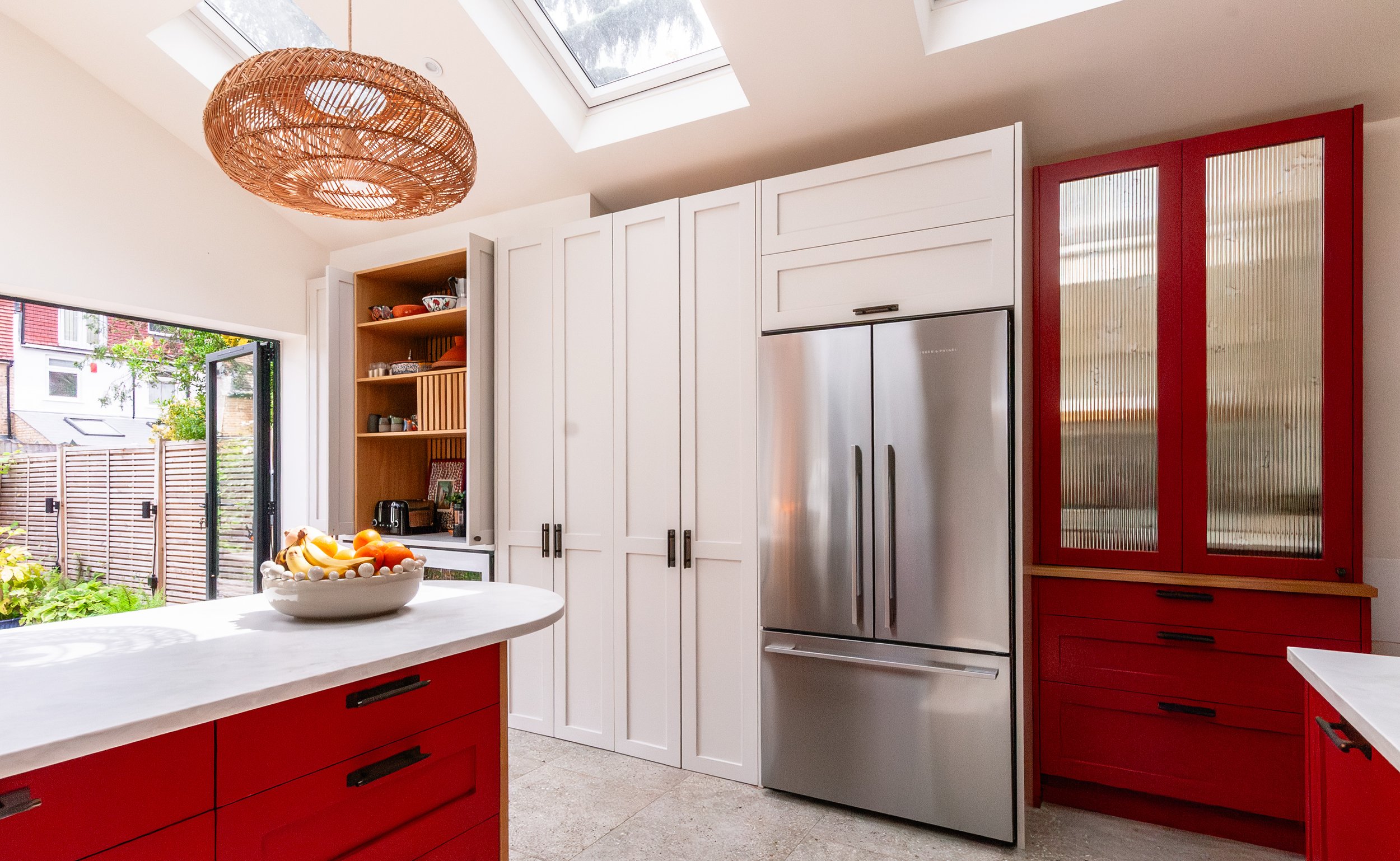 Red and soft off white storage wall in a Forest Hill kitchen extension, with reeded antique mirror larder, American-style fridge freezer, rooflights and garden views
