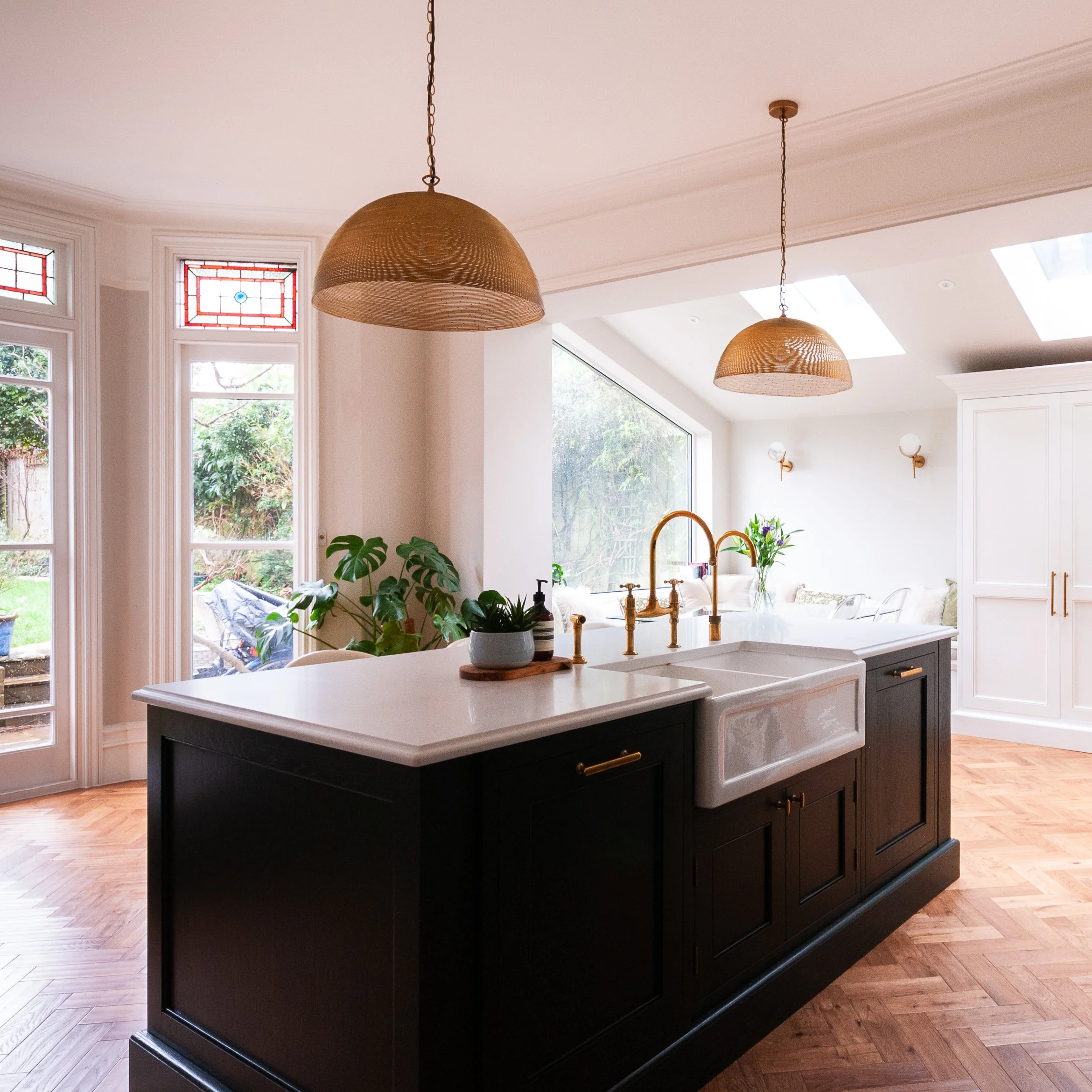 Bespoke kitchen in Herne Hill showing island sink, pendant lighting, garden views and connection to the wider living space.