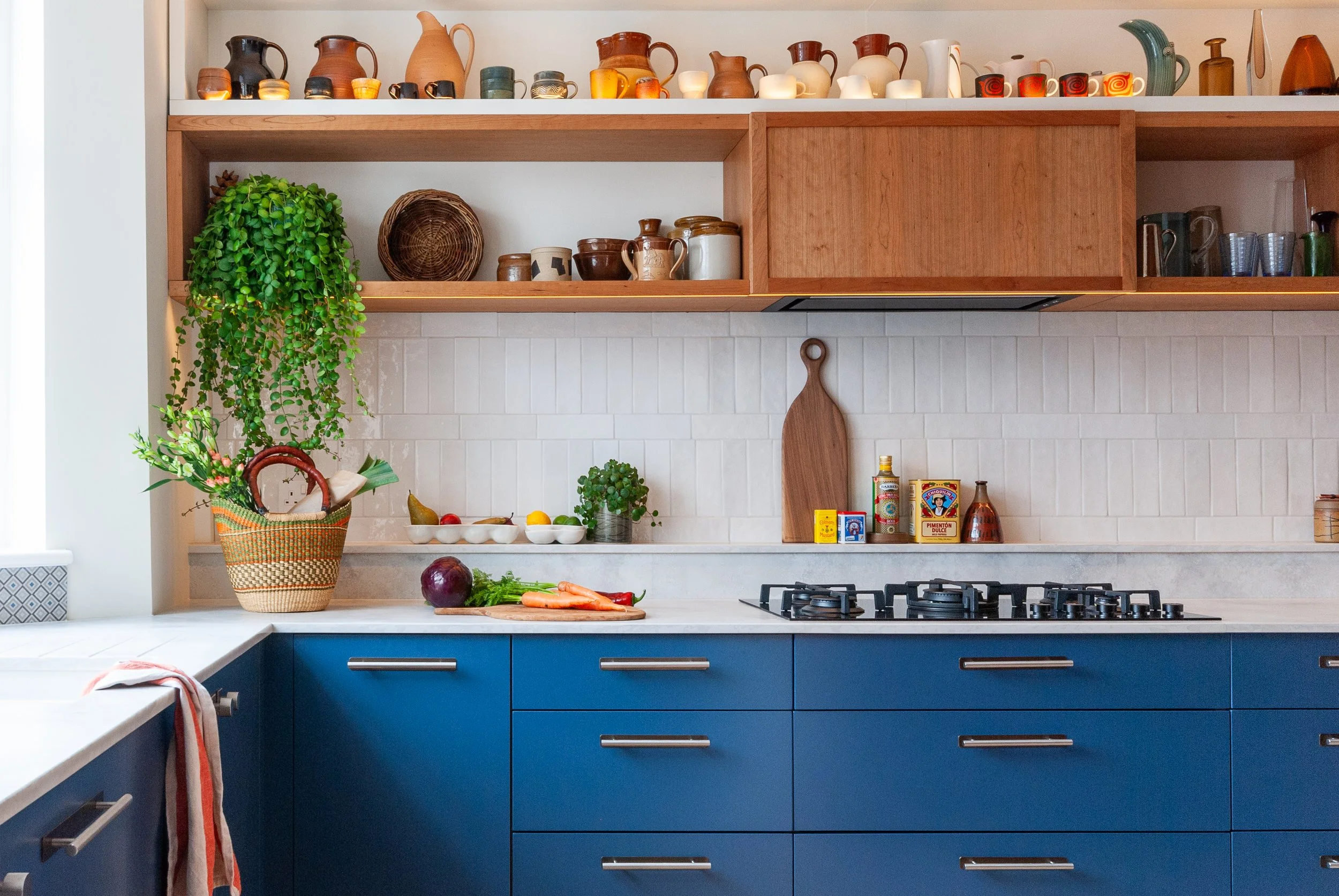 Kitchen in East Dulwich with full-length lit display shelf for pottery, open shelving, plants and personal styling details.