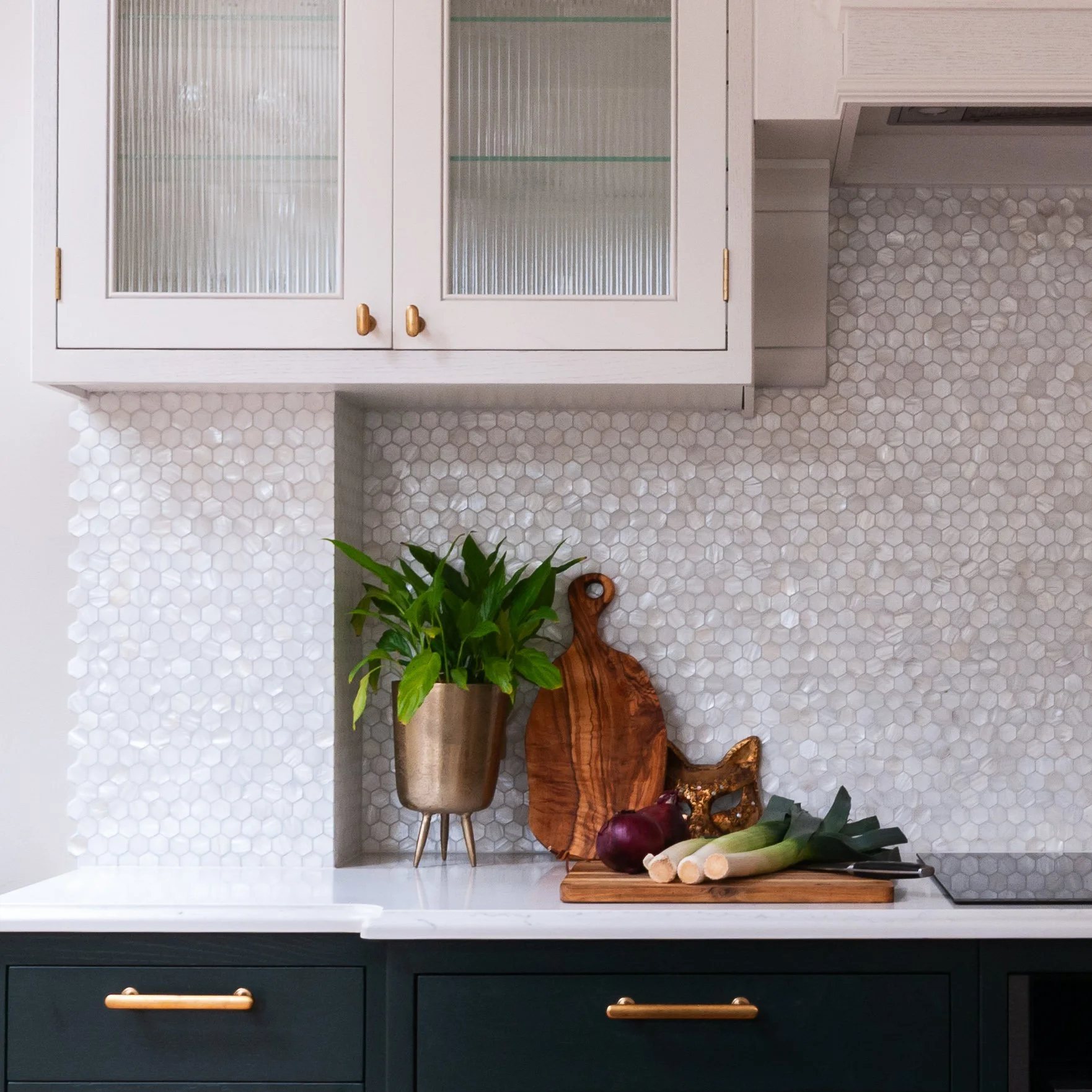 Kitchen in Herne Hill with fluted glass wall cabinets, brass handles, mother of pearl mosaic tiles and styled personal details.