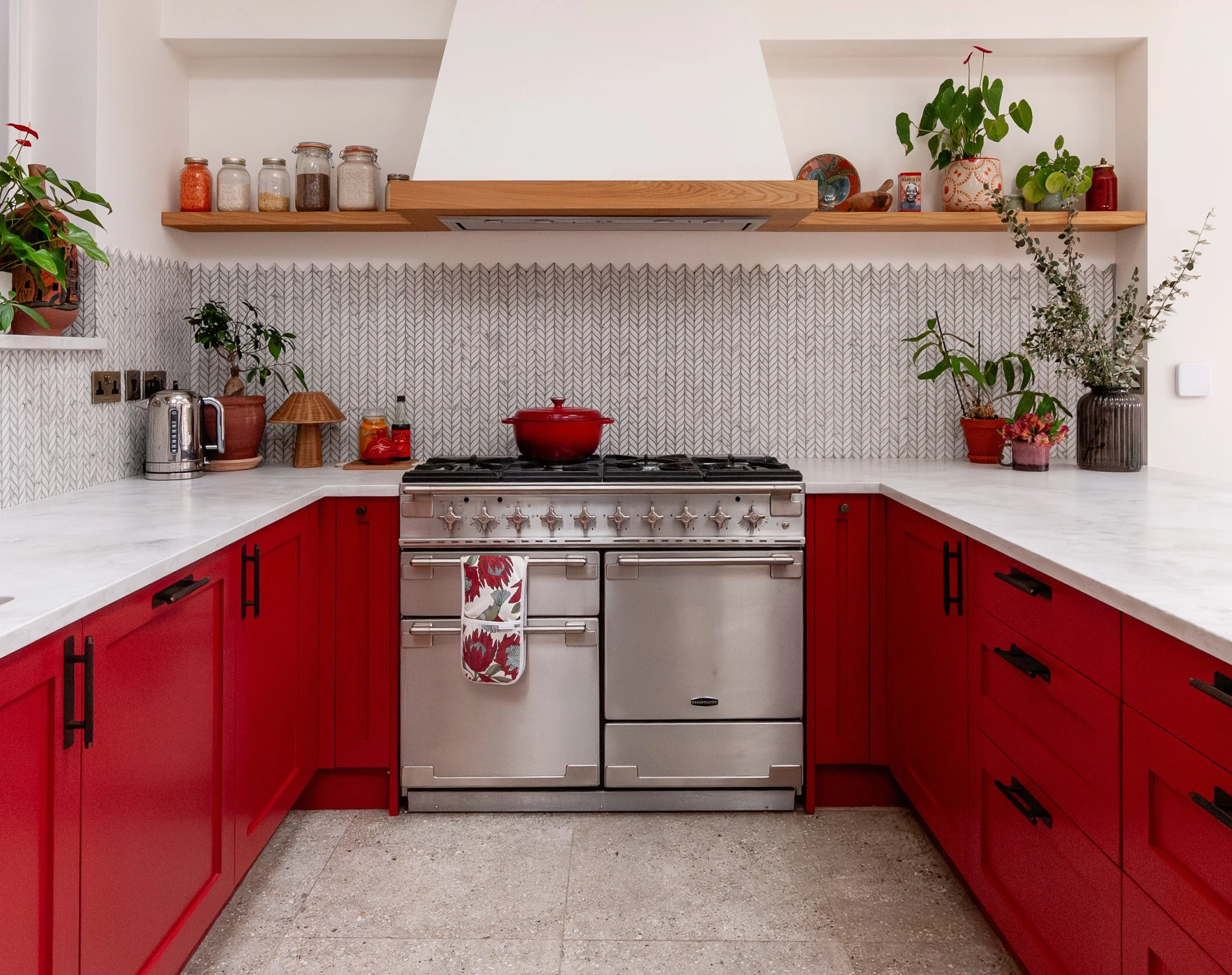 Red U-shaped kitchen in Forest Hill with range cooker, bespoke extractor canopy, oak shelf and patterned splashback tiles