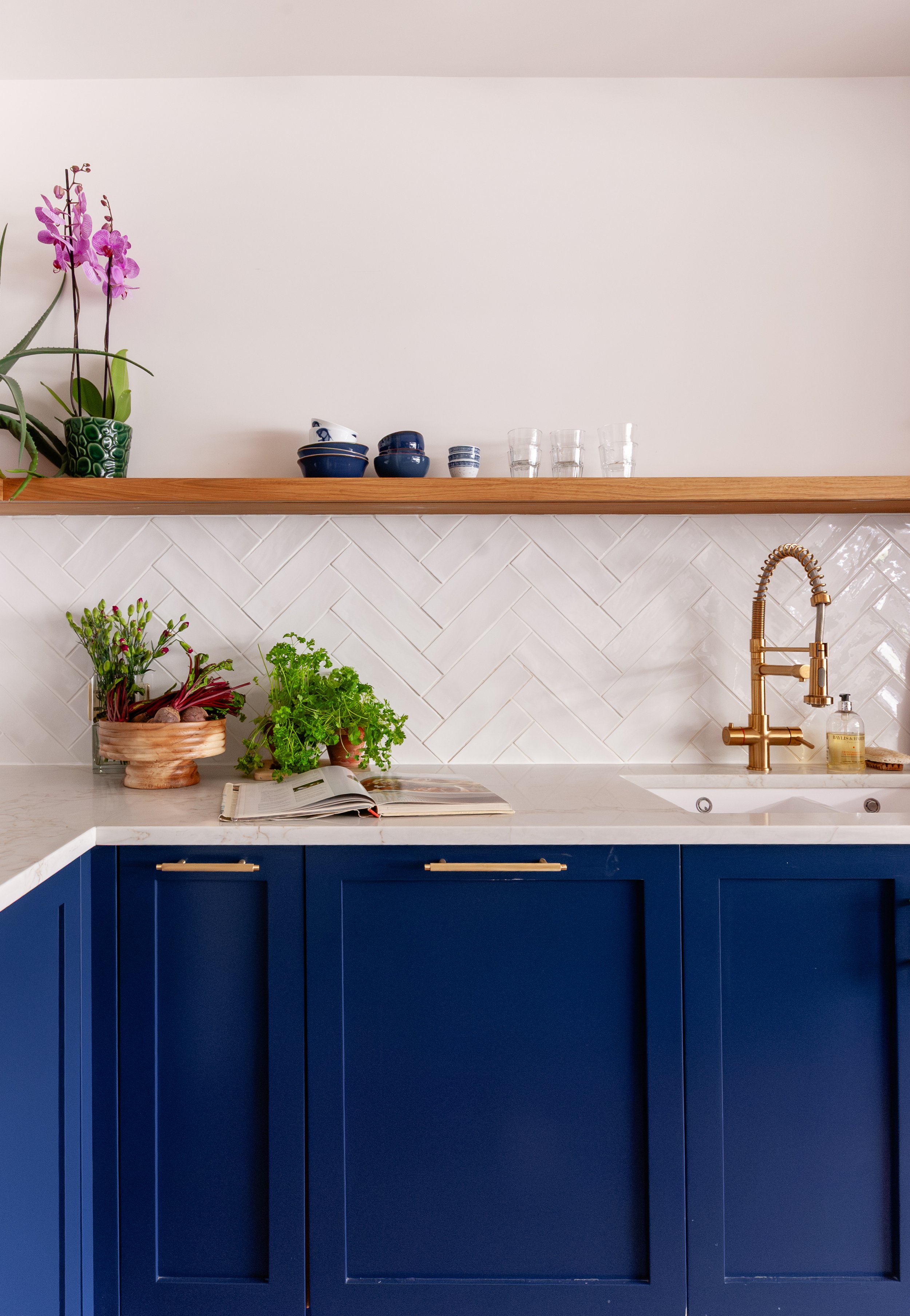 Blue kitchen cabinetry with brass tap, open shelf and herringbone tiled splashback in Beckenham