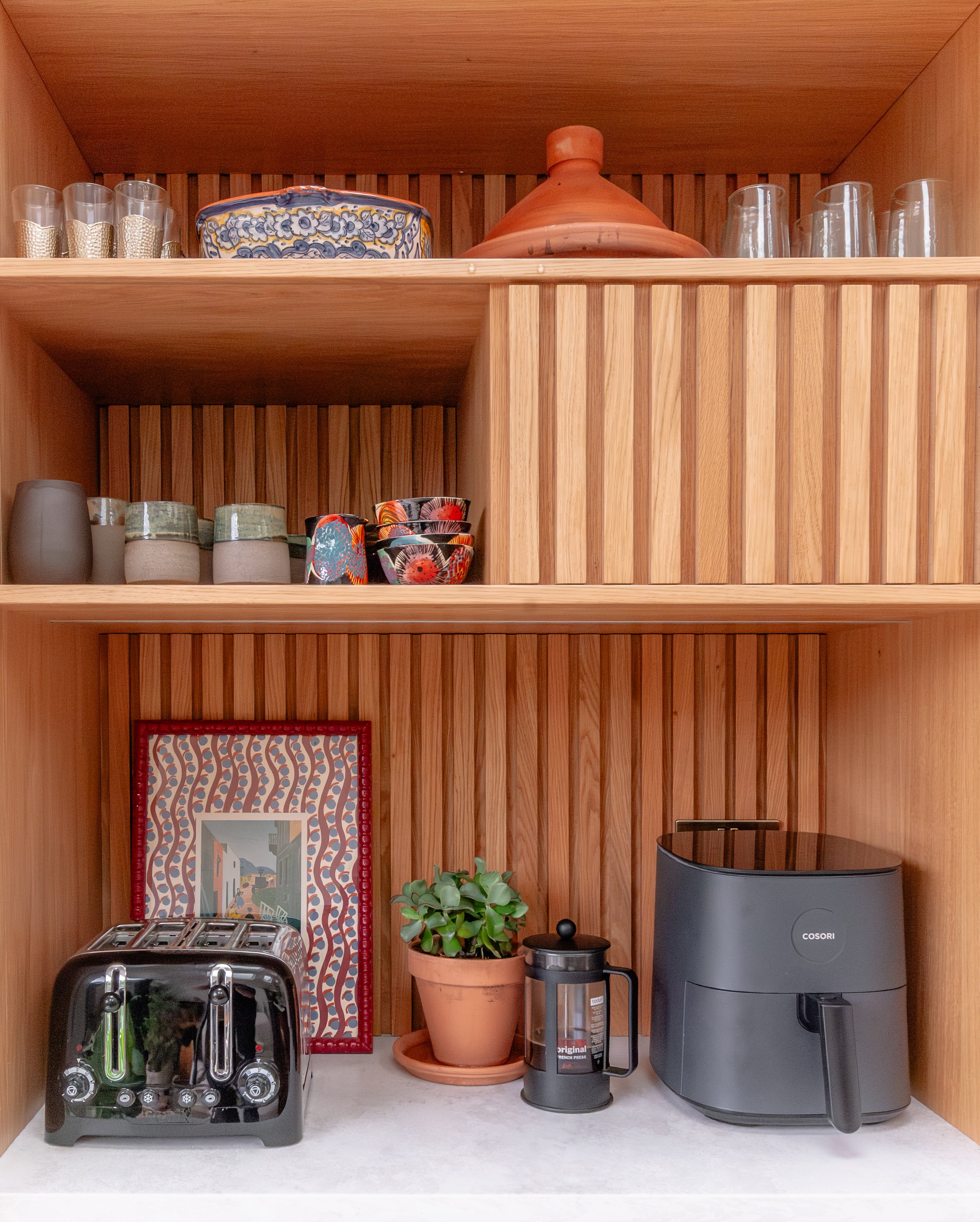 Oak breakfast cupboard in a Forest Hill kitchen extension, with fluted timber detailing, stone worktop, open shelving, pottery and concealed appliance storage
