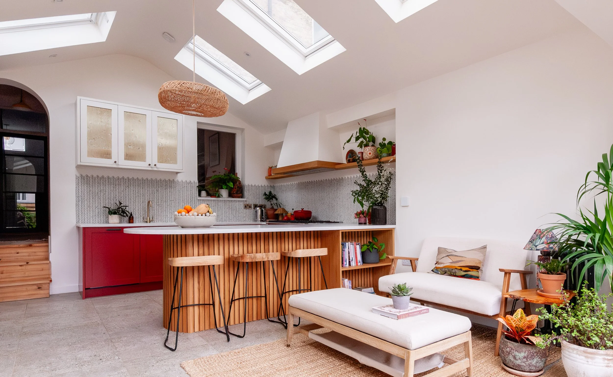 Red and oak kitchen extension in Forest Hill, South East London, designed for indoor-outdoor living with curved peninsula seating and a relaxed garden-facing seating area