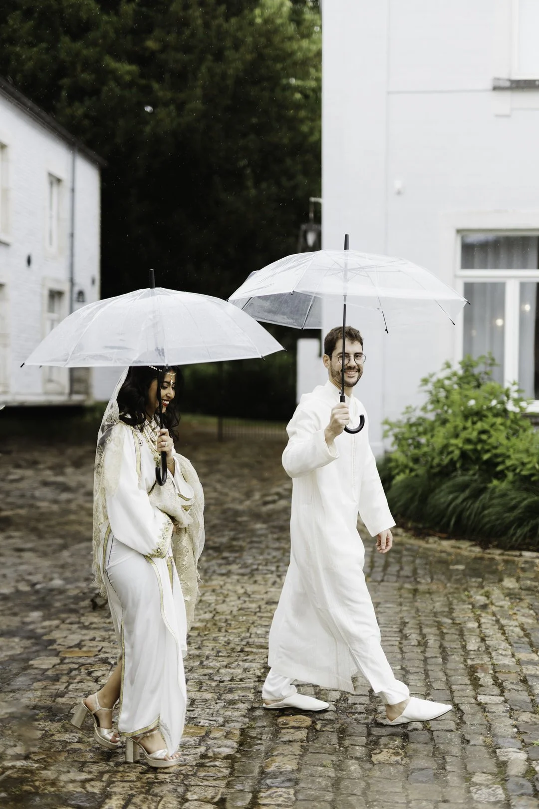 Couple de mariés sortent de la cérémonie en habit traditionnels marocains avec des parapluies en souriant