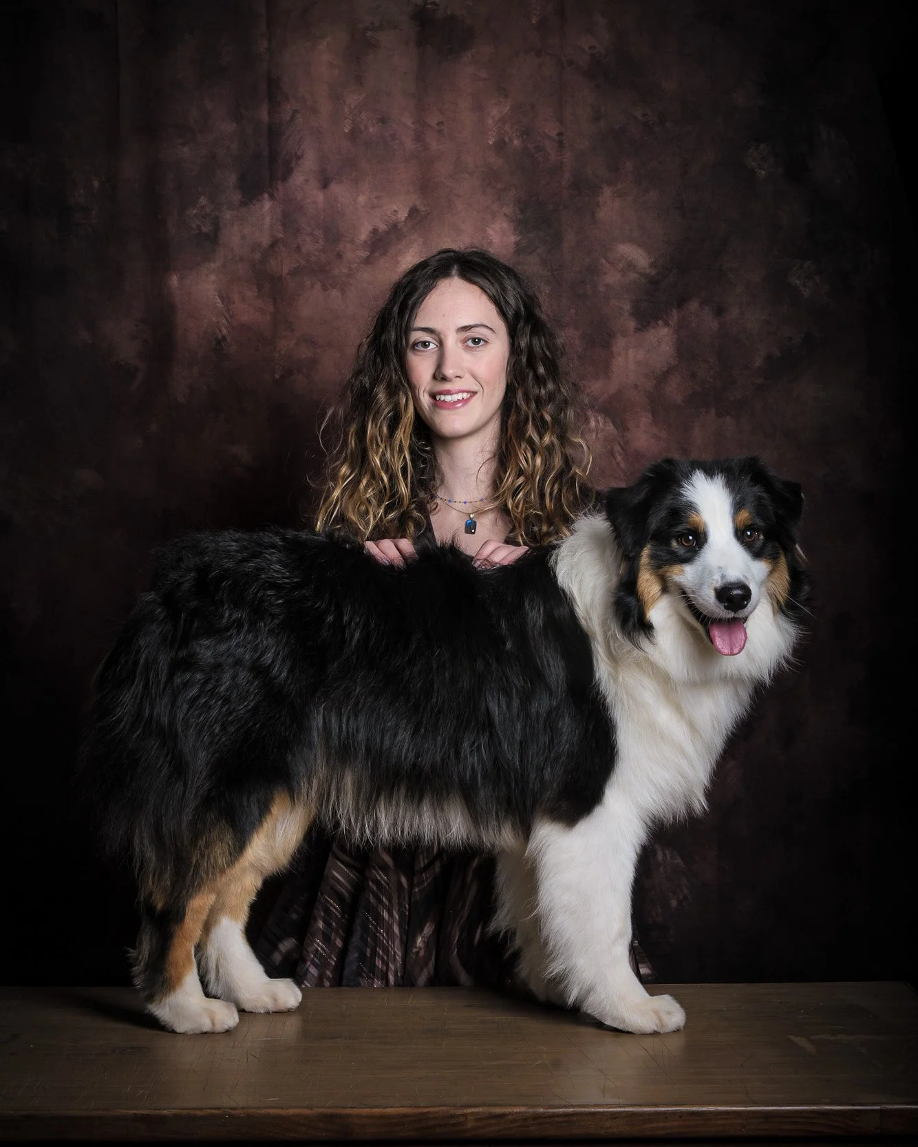 Ritratto in studio di cane Australian Shepherd in posa da show accanto alla proprietaria, su sfondo pittorico – servizio fotografico pet a Milano Sud, Corsico, Assago e Cesano Boscone.