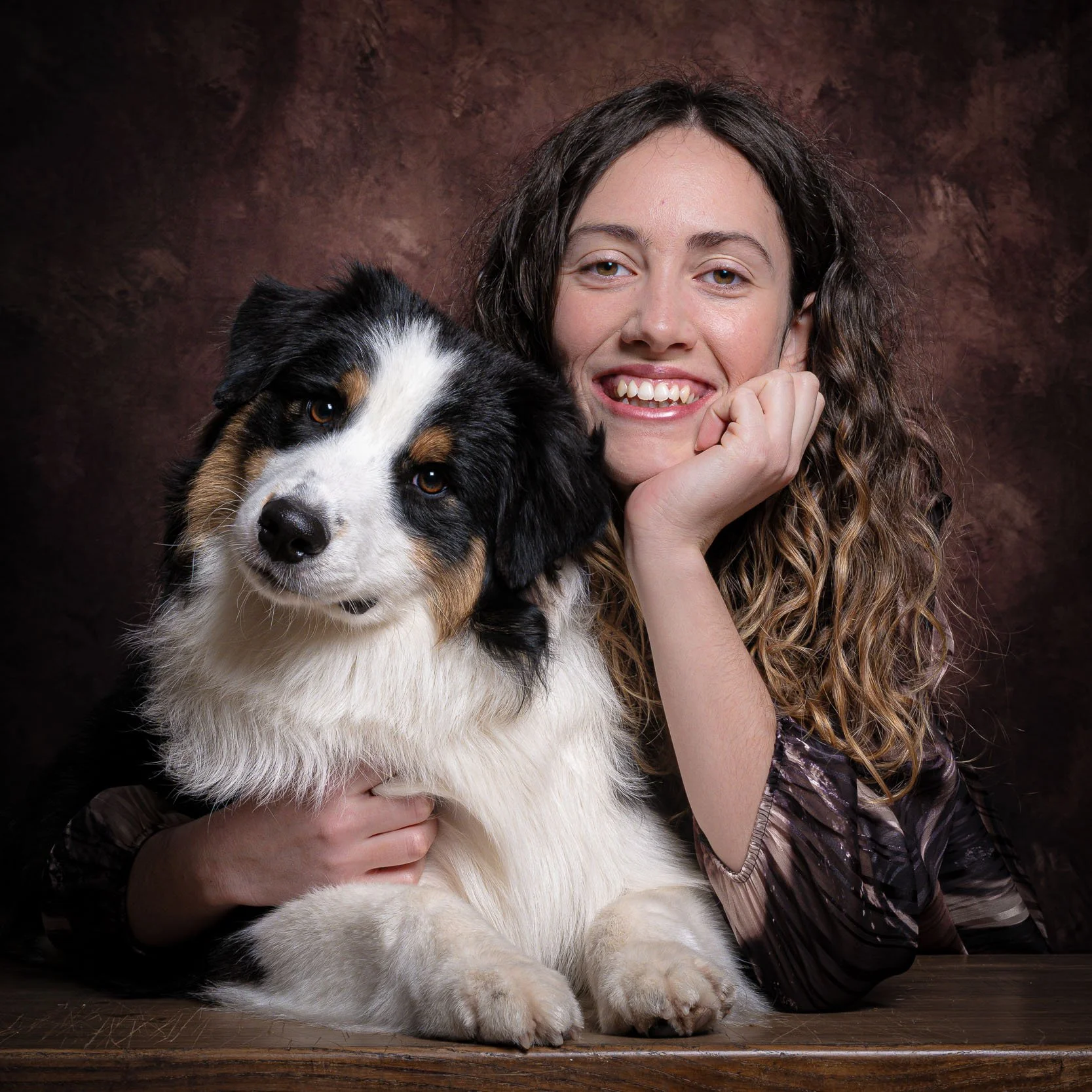 Ritratto in studio di cane Australian Shepherd abbracciato dalla proprietaria, in una posa affettuosa su sfondo pittorico – servizio fotografico pet a Milano Sud, Trezzano sul Naviglio, Assago e Buccinasco.