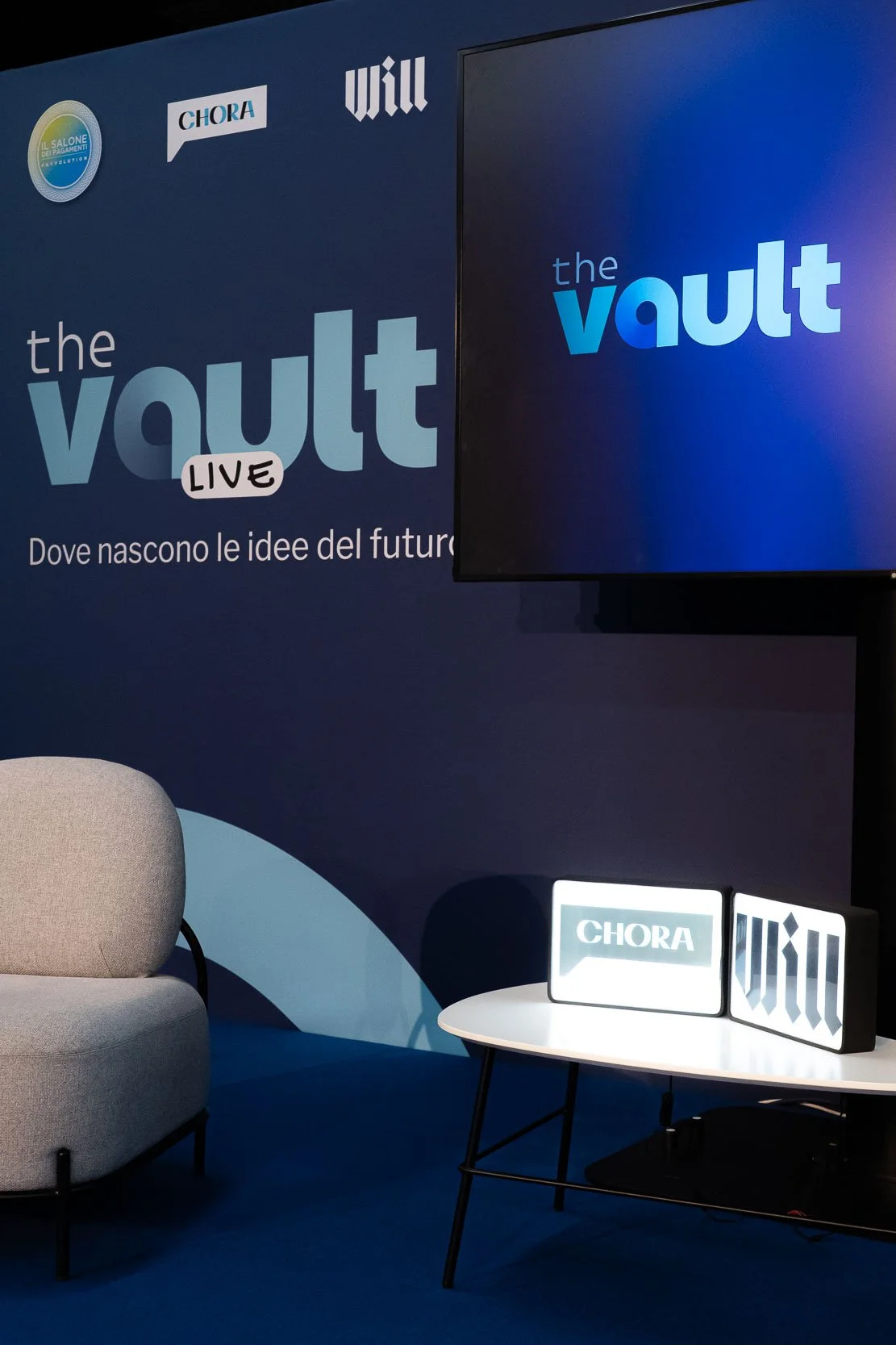 Dettaglio del set di The Vault Live di Will e Chora Media al MiCo di Milano, con monitor, pannello grafico e area sedute pronte per l’evento.
