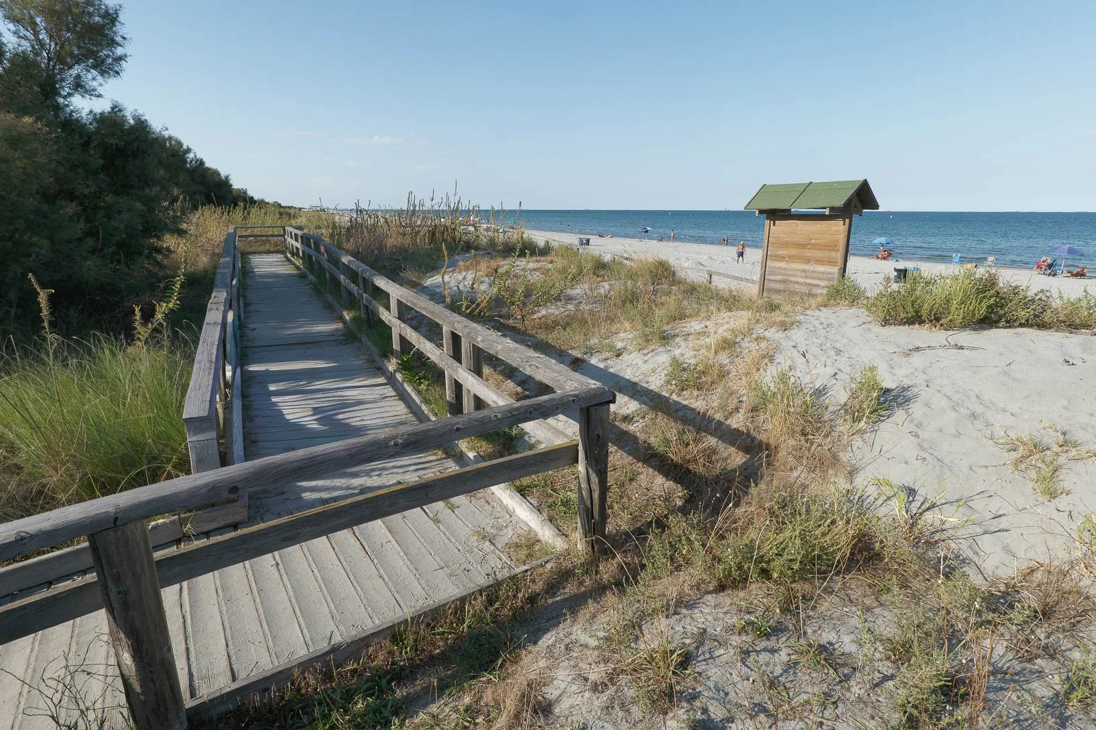 Passerella in legno tra le dune di Ravenna, con la spiaggia e il mare sullo sfondo.