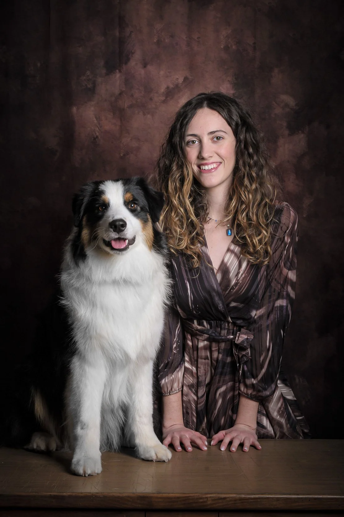 Ritratto in studio di cane Australian Shepherd seduto accanto alla proprietaria, su sfondo pittorico – servizio fotografico pet a Milano Sud, Buccinasco, Corsico e Assago.