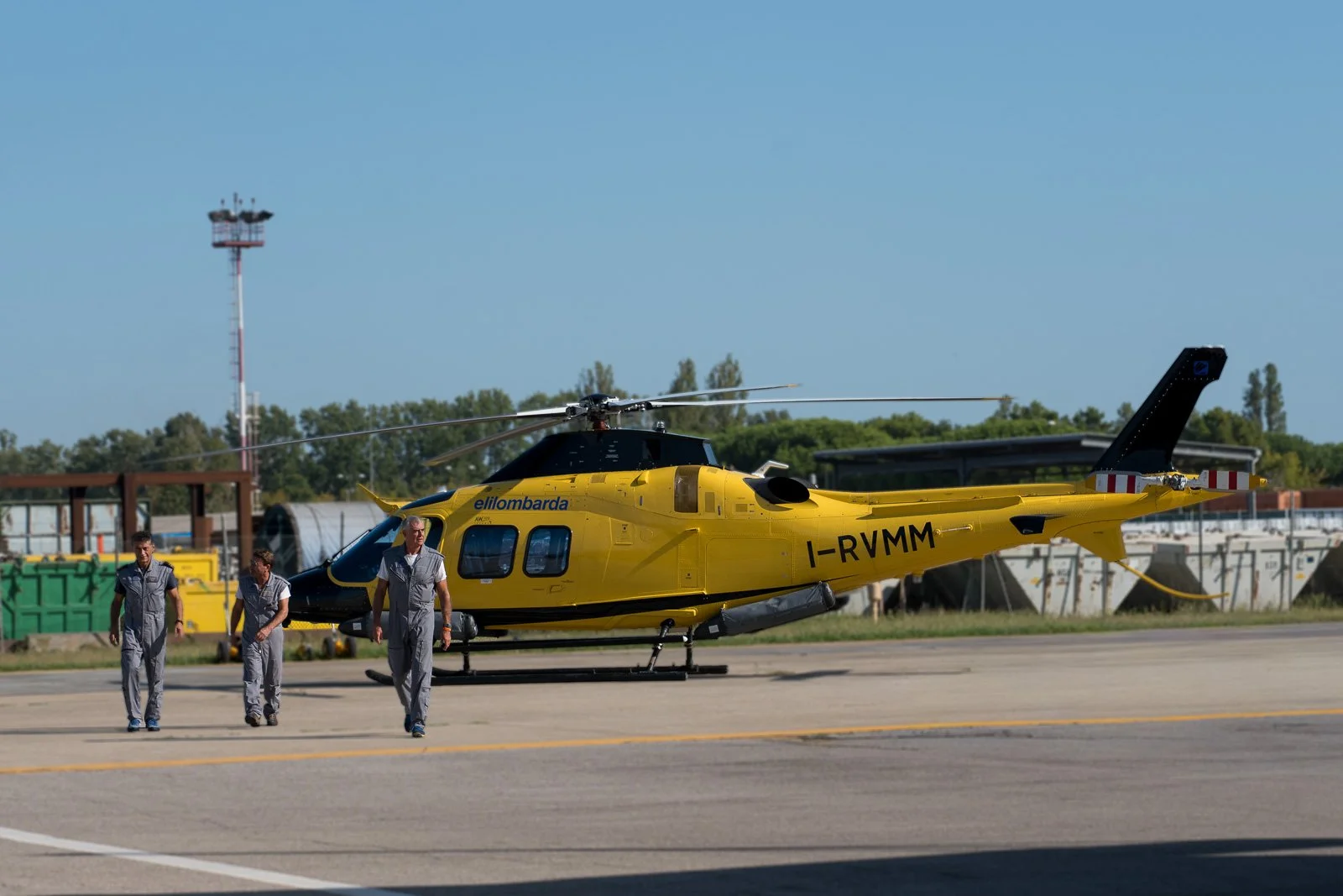 Tre membri dell’equipaggio camminano verso l’obiettivo, con l’elicottero Elilombarda alle spalle.