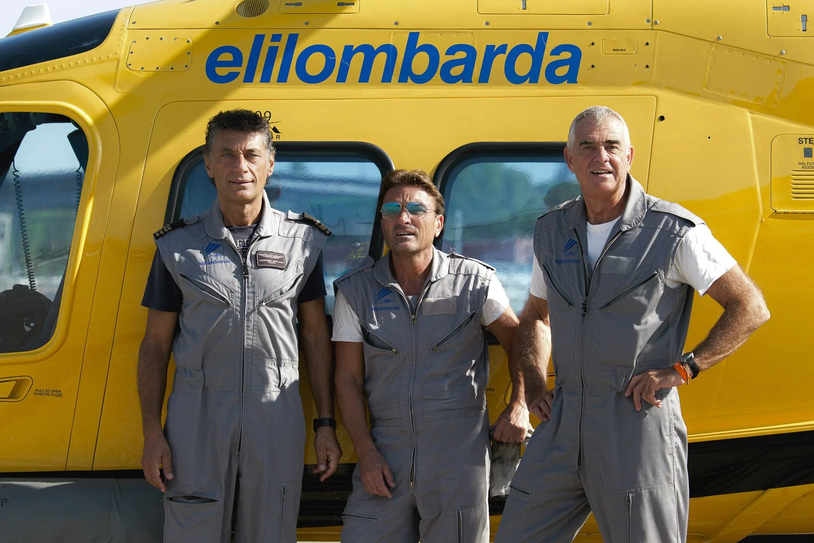 Ritratto di tre membri dell’equipaggio davanti alla fusoliera gialla dell’elicottero, sotto la scritta Elilombarda.