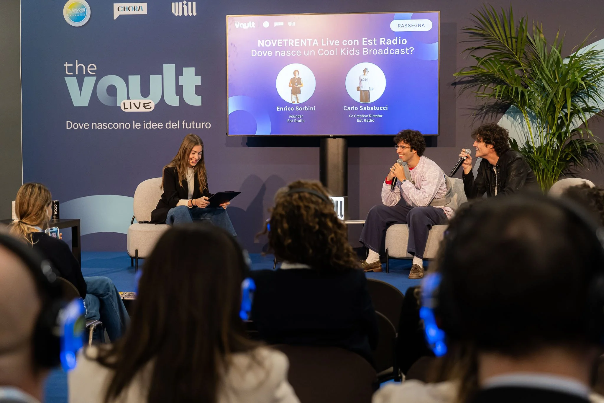 Pubblico in ascolto durante il talk “NOVETRENTA Live” con Est Radio sul palco di The Vault Live al MiCo di Milano, con moderatrice e ospiti in dialogo.
