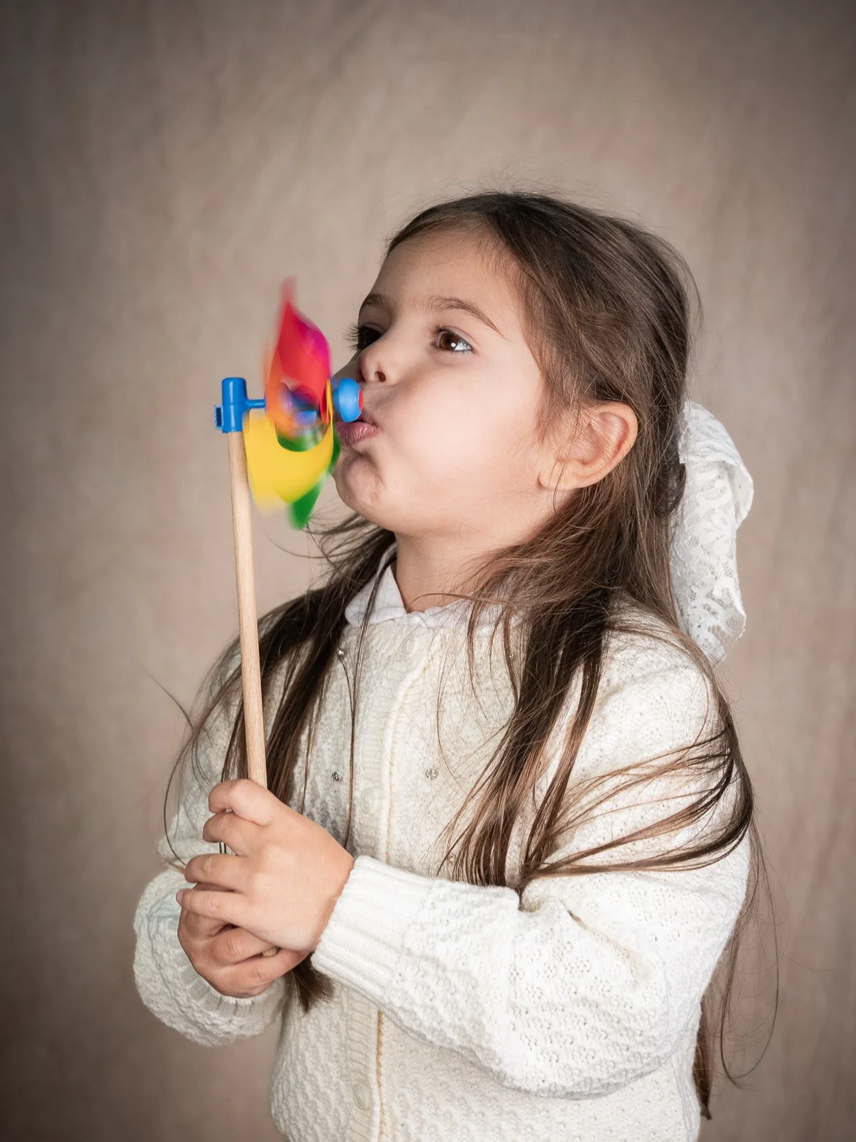 Ritratto in studio di bambina che soffia su una girandola colorata, realizzato con luce morbida – servizio fotografico di famiglia a Milano Sud, Buccinasco, Corsico e Assago.
