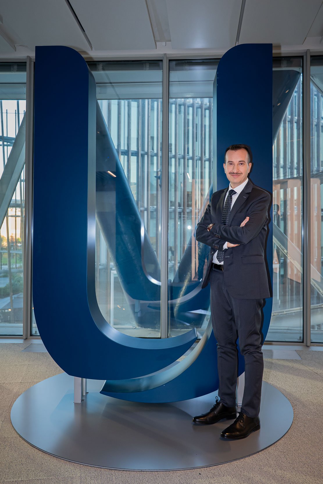 Ritratto corporate negli uffici Unipol di Milano, con il soggetto posato davanti al grande logo aziendale prima della registrazione del podcast.
