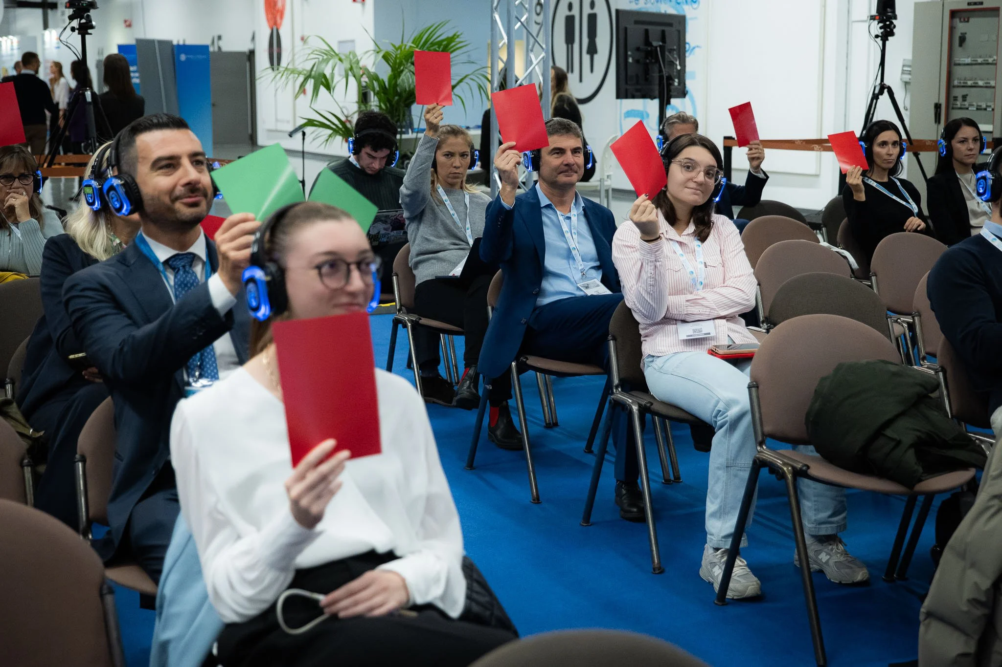 Il pubblico partecipa attivamente alla sessione interattiva di The Vault a MiCo Milano, alzando cartellini rossi e verdi durante una fase di votazione live.