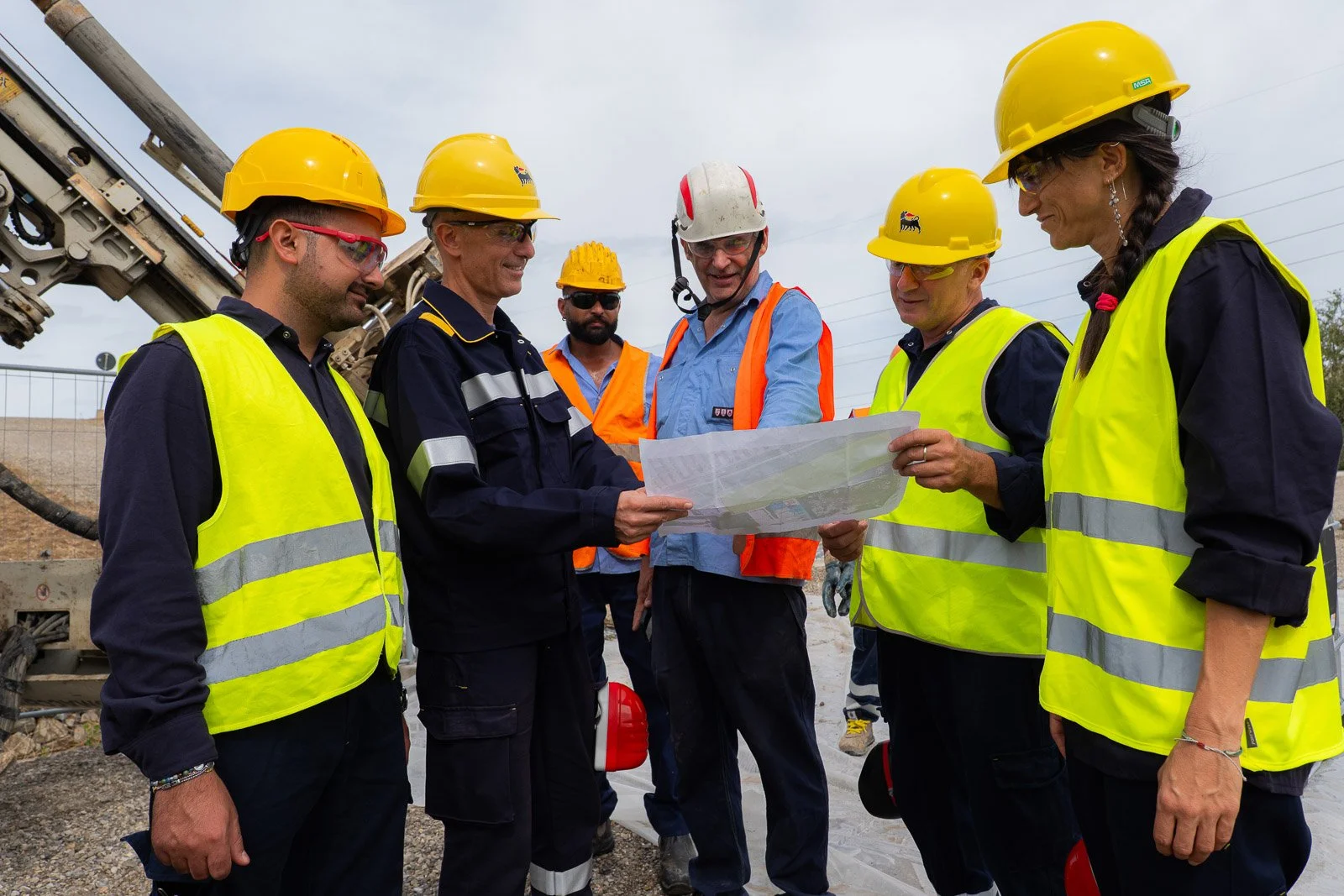 Gruppo di operatori riunito attorno a una planimetria, con i macchinari di cantiere sullo sfondo.