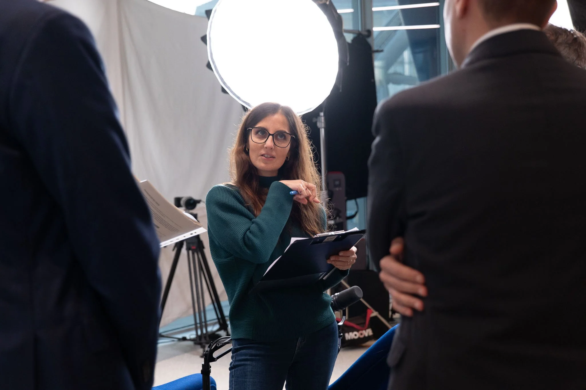 Coordinamento del team tecnico durante il briefing sul set del podcast Unipol negli uffici aziendali di Milano, con luci e attrezzatura di produzione.
