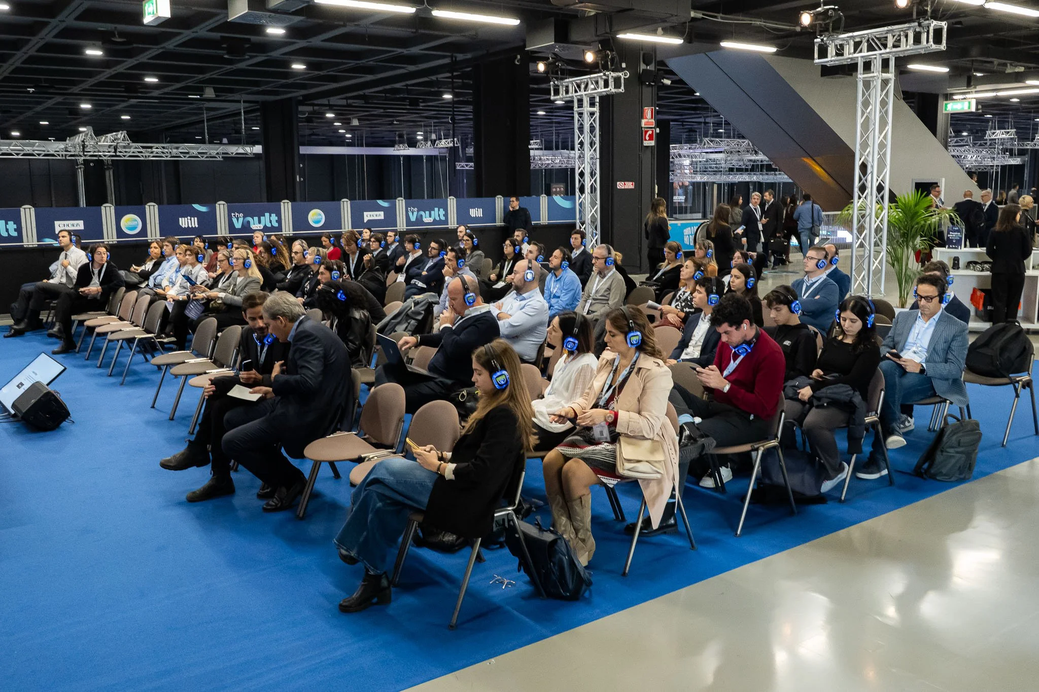 Il pubblico assiste alle conferenze di The Vault Live al MiCo di Milano, con cuffie per l’ascolto e area eventi allestita da Will Media e Chora Media. Reportage fotografico dell’evento corporate.
