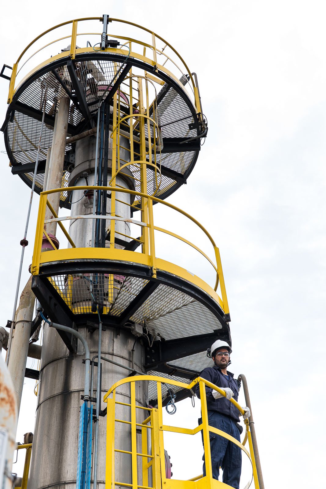 Operatore su una piattaforma di una torre industriale, tra scale verticali e parapetti gialli.