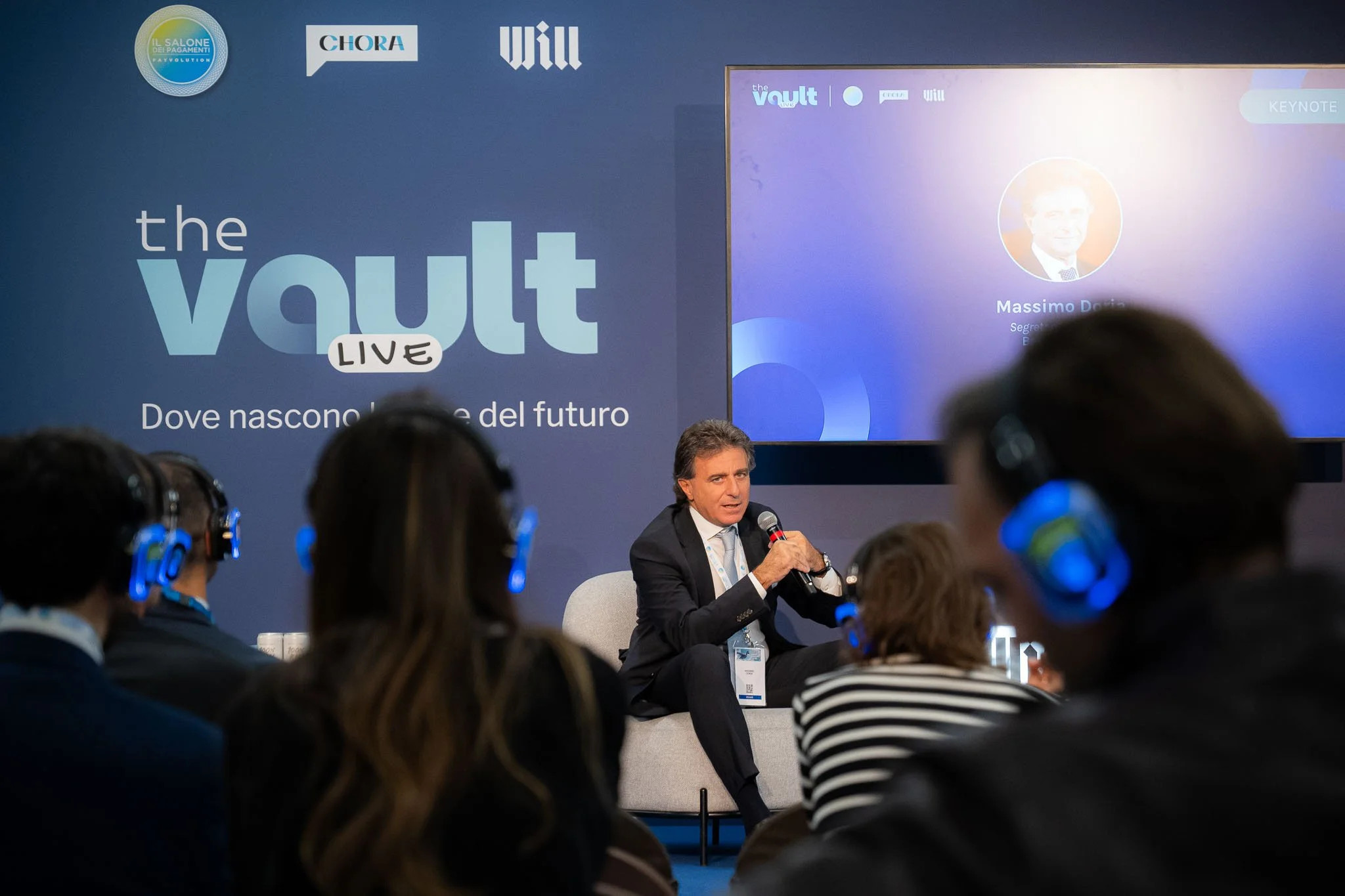 Intervento istituzionale sul palco di The Vault Live durante la keynote, con pubblico in ascolto tramite cuffie silent conference.
