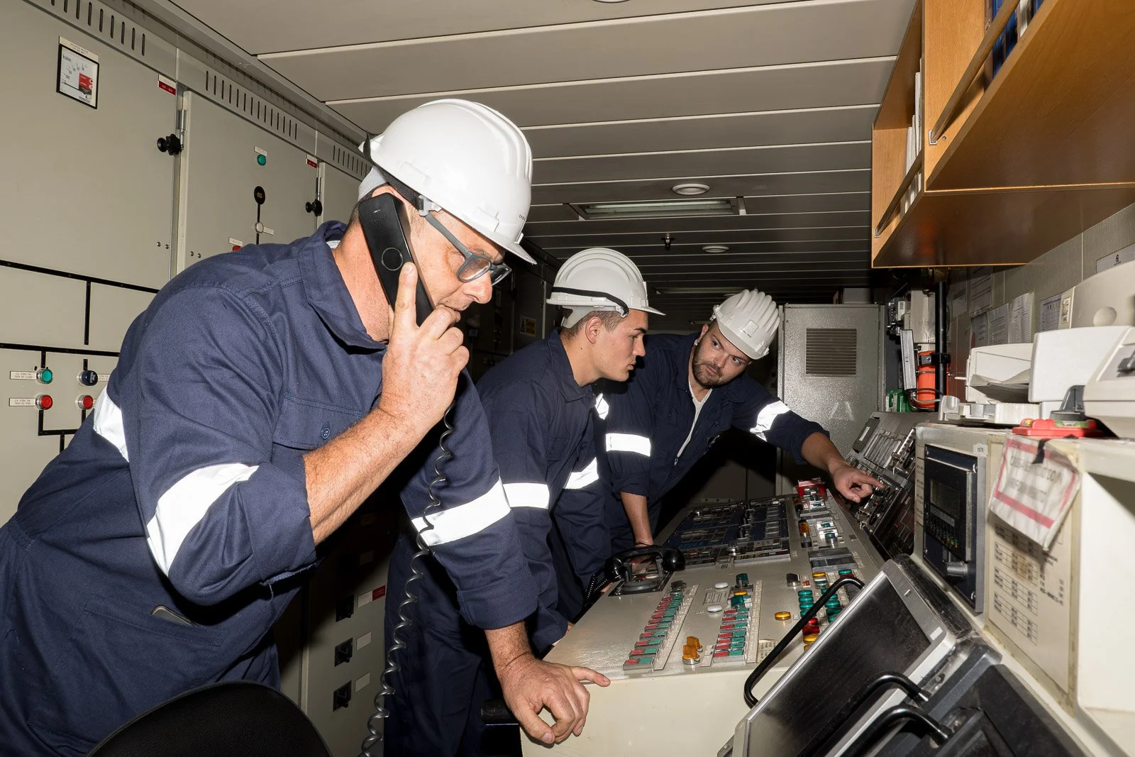 Tre operatori nella sala controllo: uno parla al telefono mentre un collega indica il pannello comandi.