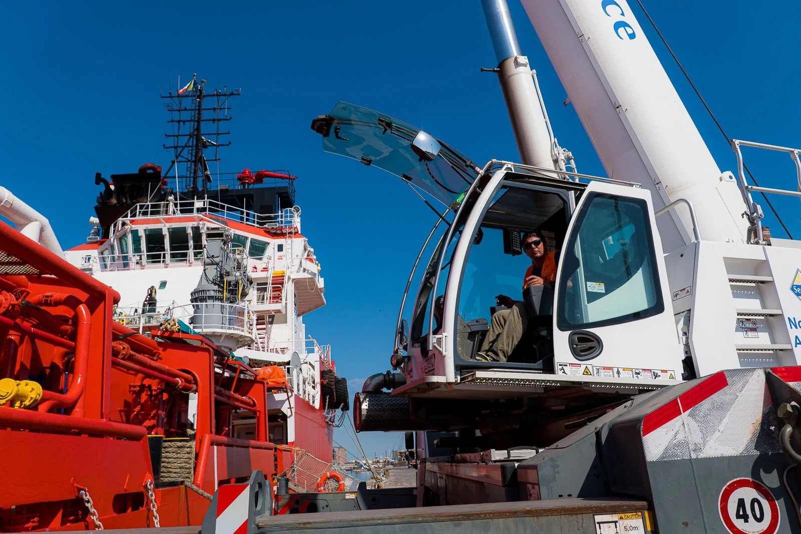 Gruista ai comandi dell’autogru in banchina, accanto allo scafo rosso della nave Asso Ventiquattro.