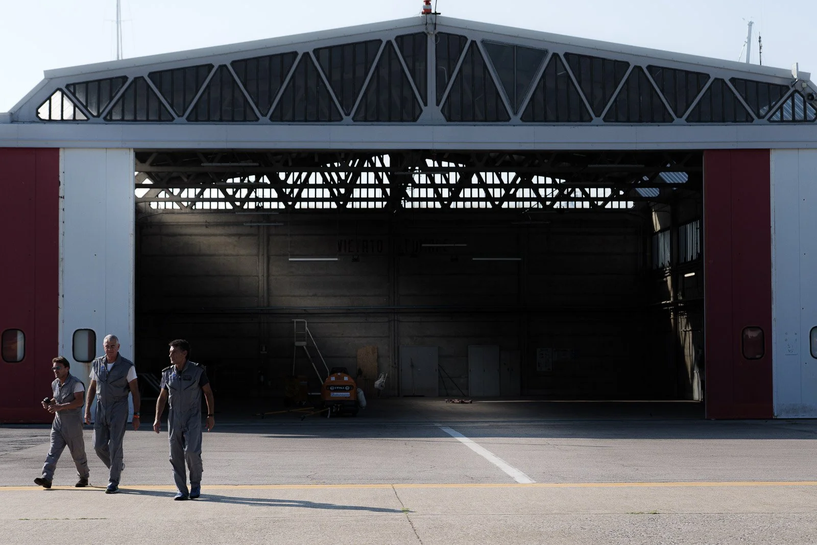 Tre membri dell’equipaggio in tuta grigia camminano davanti all’ingresso aperto dell’hangar.