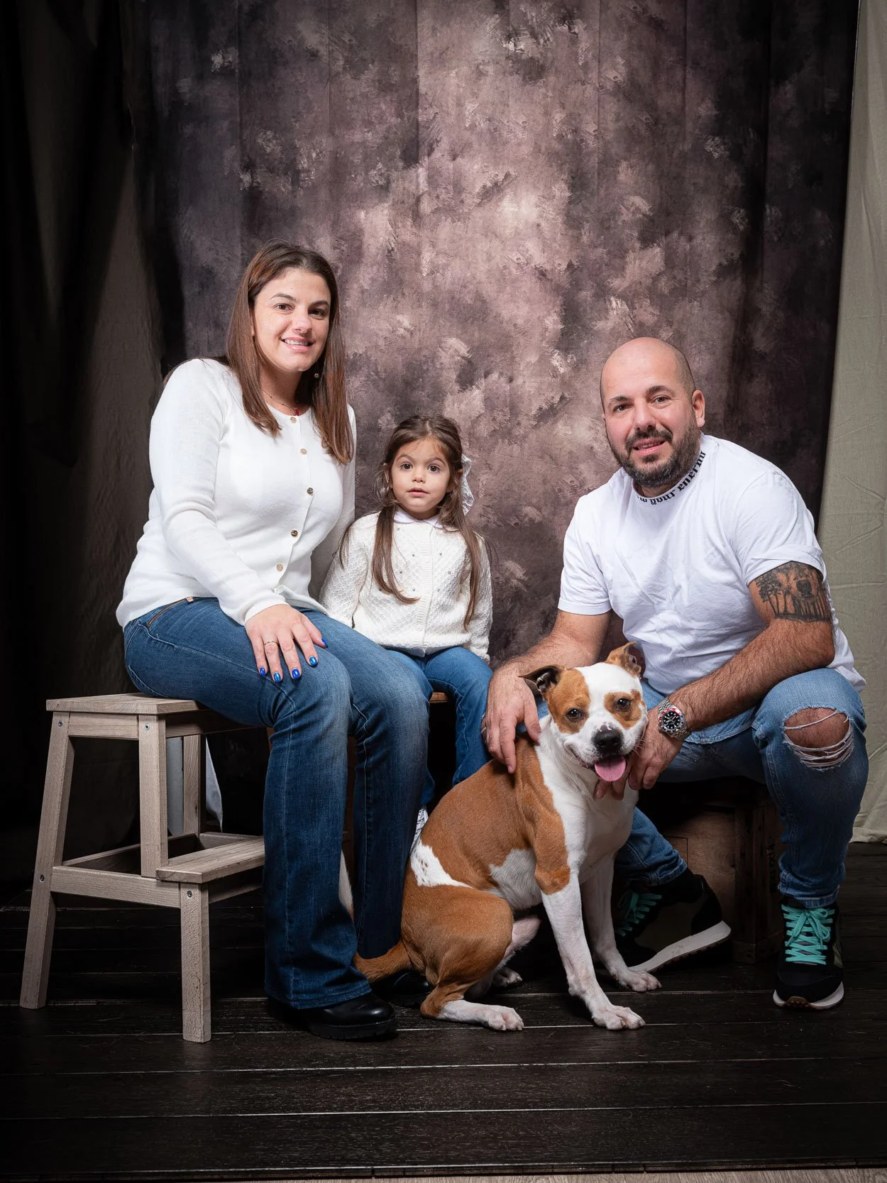 Ritratto di famiglia in studio con mamma, papà, bambina e cane in posa completa su sfondo artistico – servizio fotografico di famiglia a Milano Sud, Buccinasco, Corsico e Trezzano sul Naviglio.
