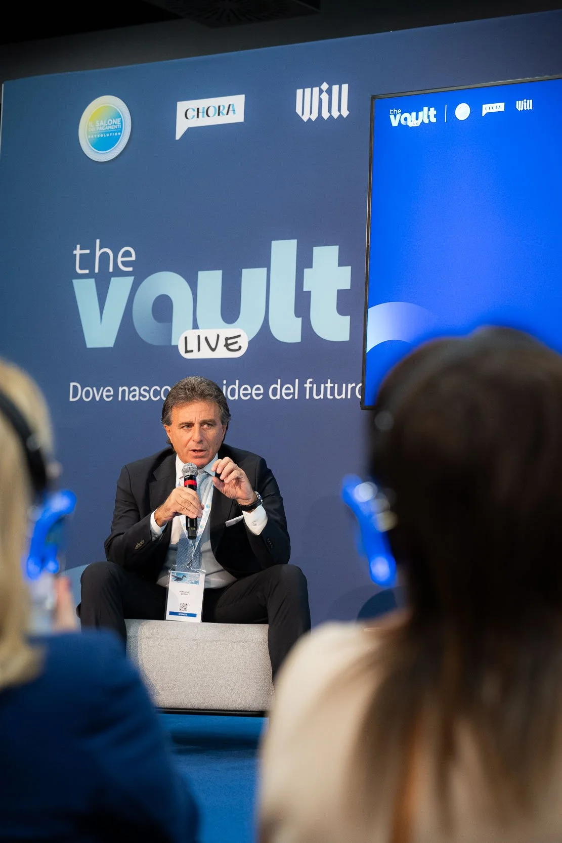 Relatore sul palco di The Vault Live durante una sessione keynote, con pubblico in ascolto tramite cuffie silent conference.
