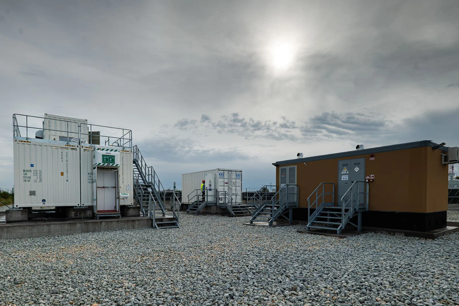 Moduli prefabbricati e container con scale e passerelle metalliche nell’area dello stabilimento.