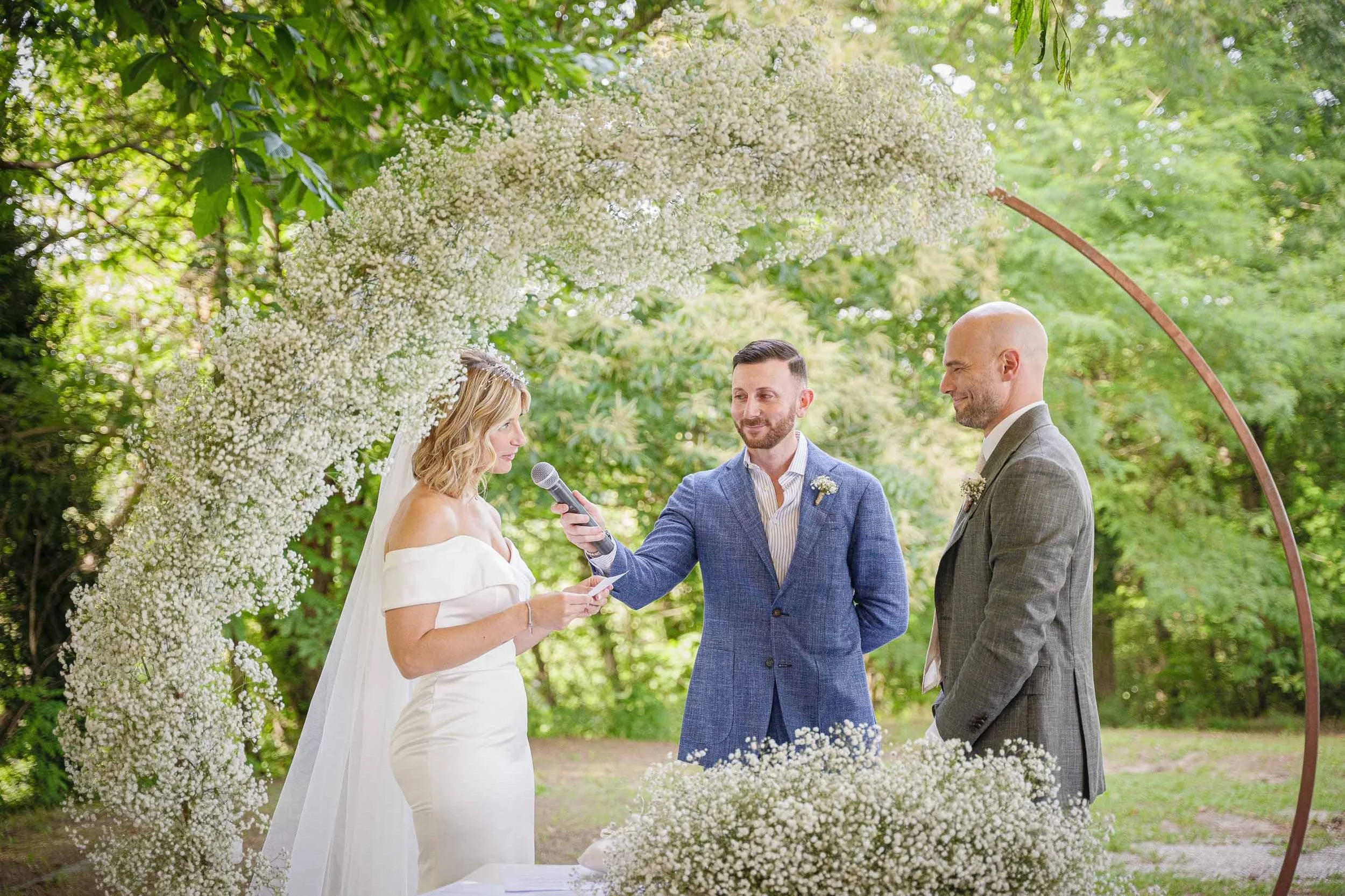Sposa che legge le proprie promesse sotto l’arco di gypsophila durante la cerimonia civile a Tenuta Montezeglio Invorio
