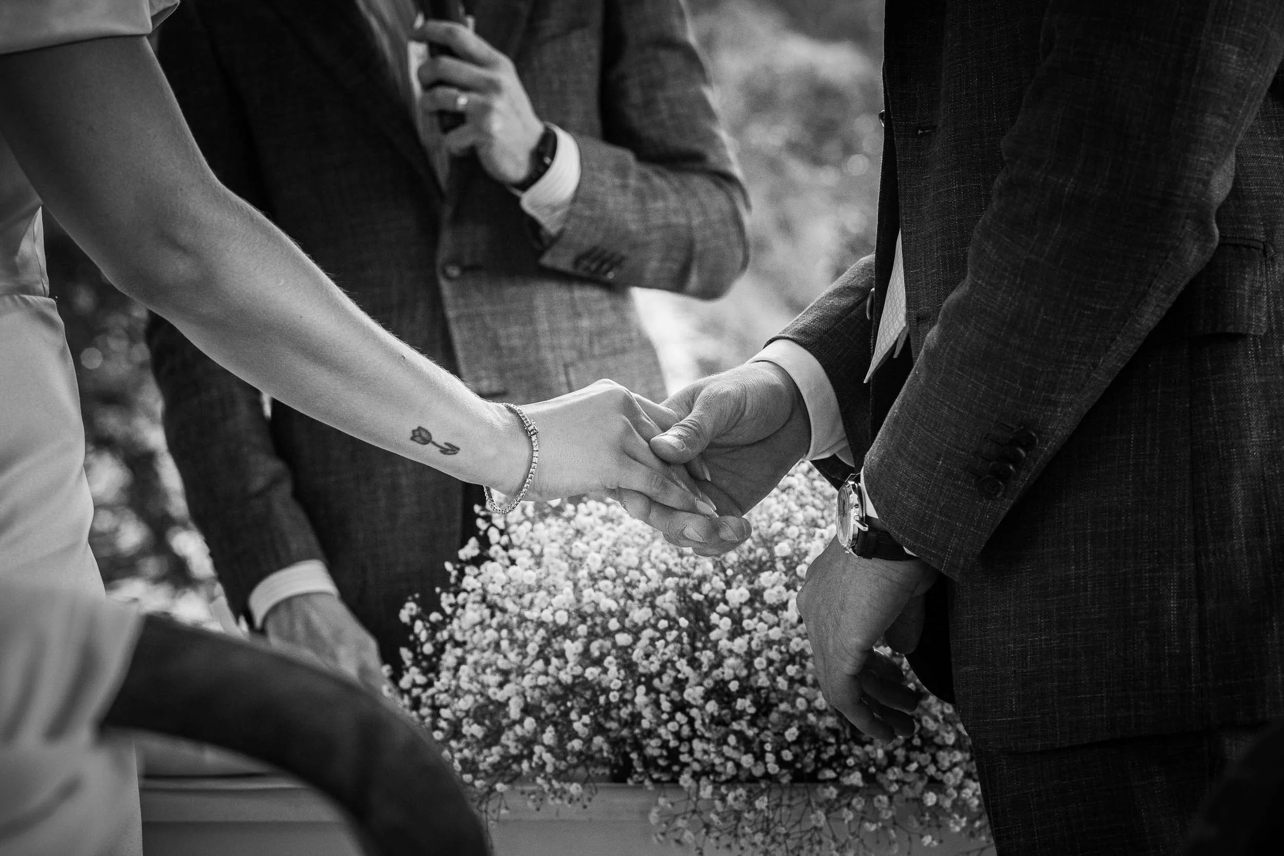 Dettaglio delle mani degli sposi intrecciate durante la cerimonia nuziale a Tenuta Montezeglio, fotografia in bianco e nero dal forte valore simbolico