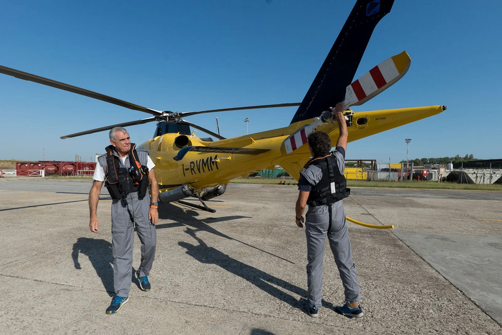 Un membro dell’equipaggio controlla il rotore di coda dell’elicottero mentre un collega cammina sul piazzale.