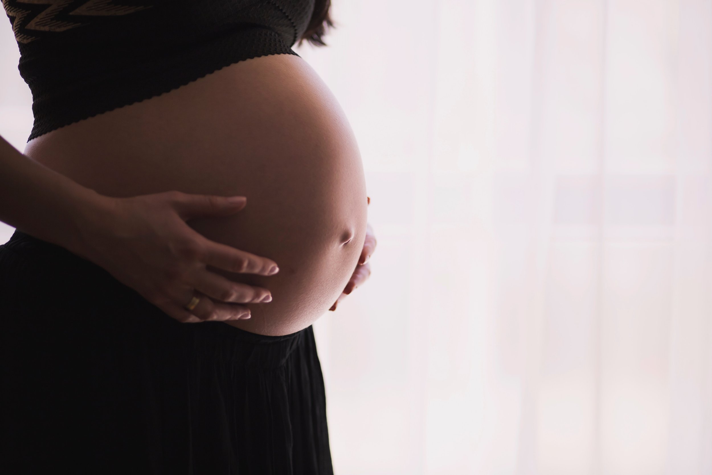 Pregnant woman gently holding her belly near a window, symbolizing safety and accuracy of non-invasive prenatal paternity testing during pregnancy