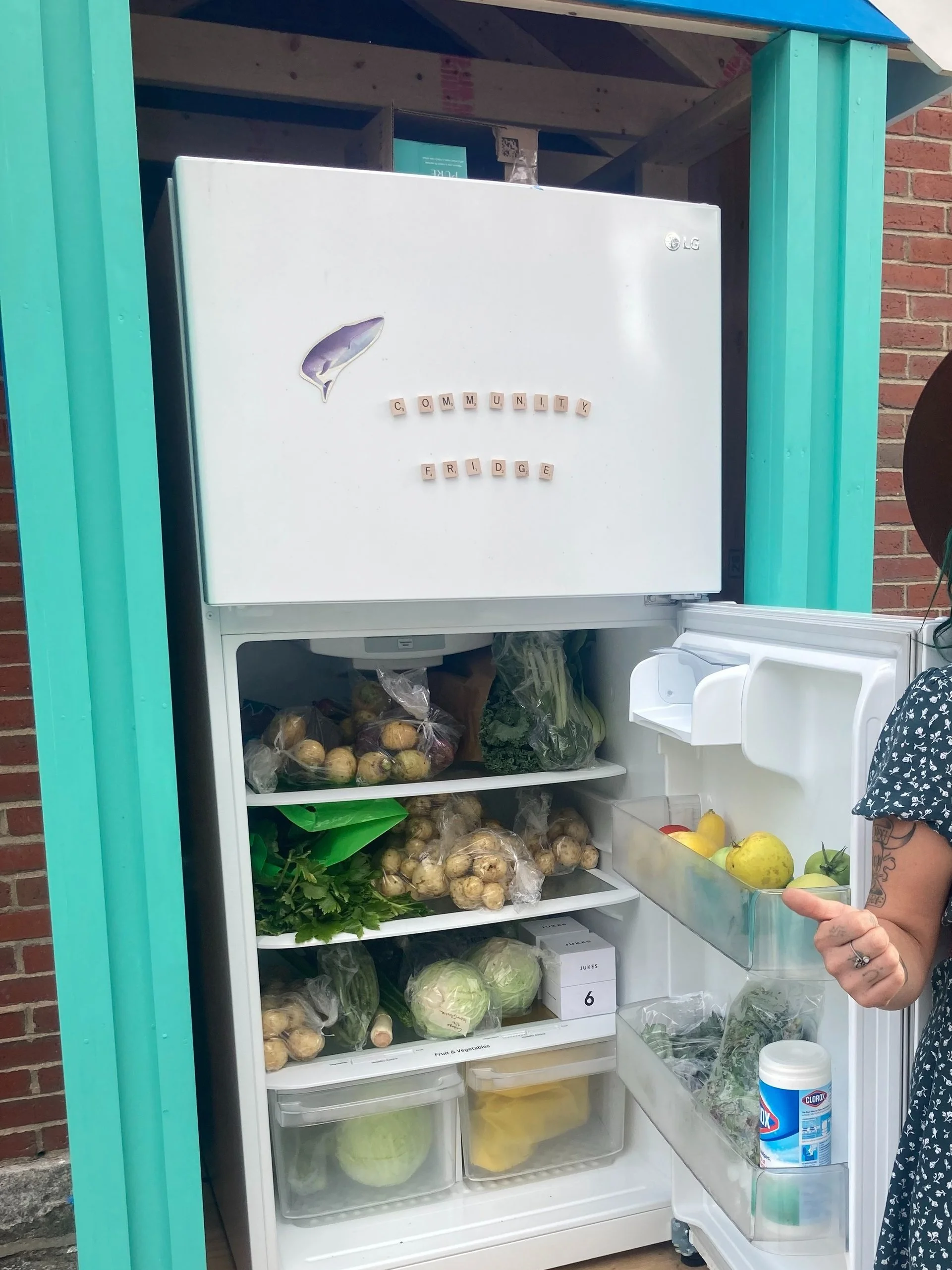a white fridge sits inside a blue hutch with the door open and it is filled withh all sorts of veggies, leafy greens and potatoes and lemons, to name a few, alongside water and containers of soup