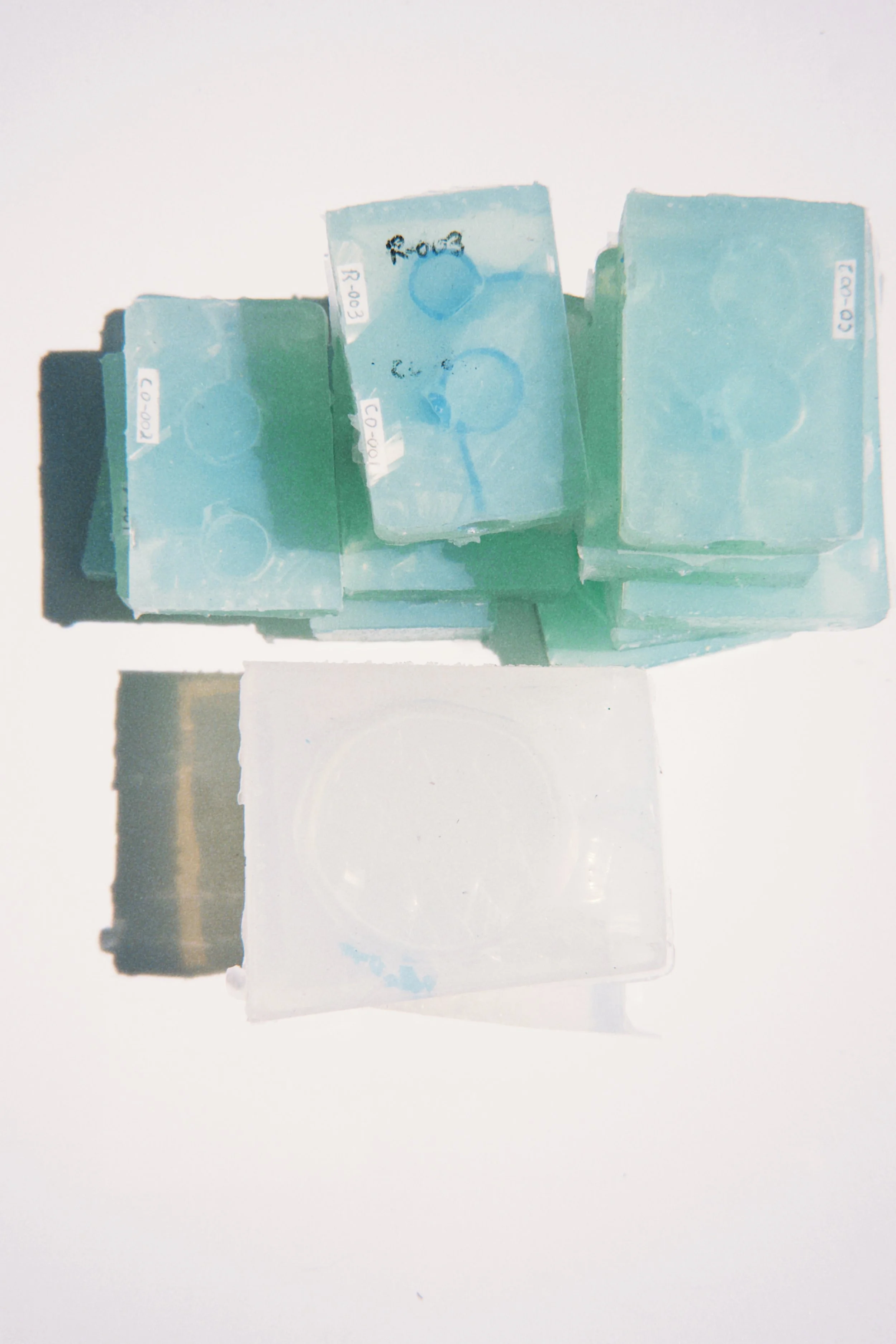 Six small blue rectangular ice packs with white labels are arranged on a white surface, with some text and drawings visible on the labels.