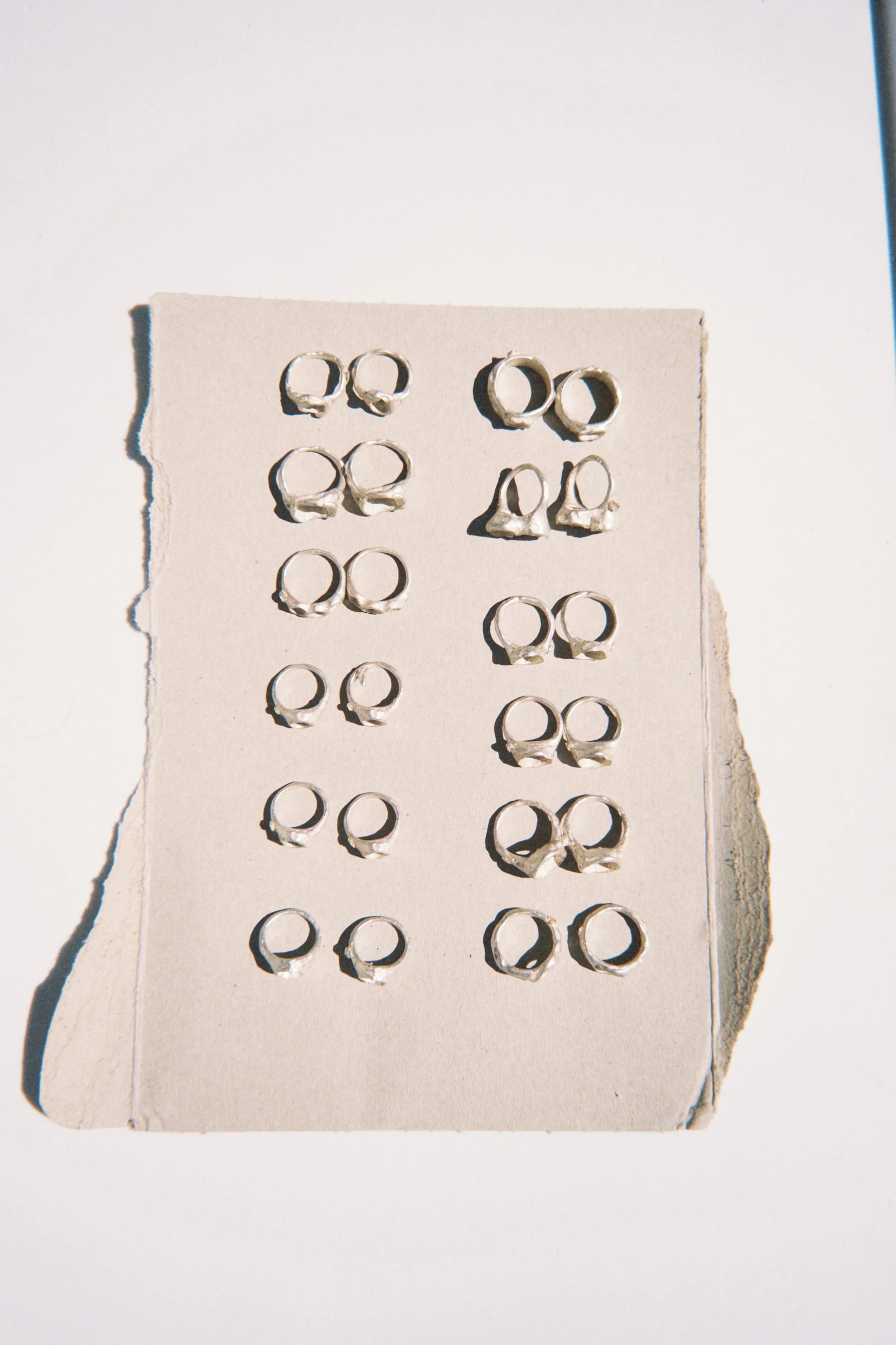 Close-up of small silver hoop earrings displayed on a torn piece of white cardboard.
