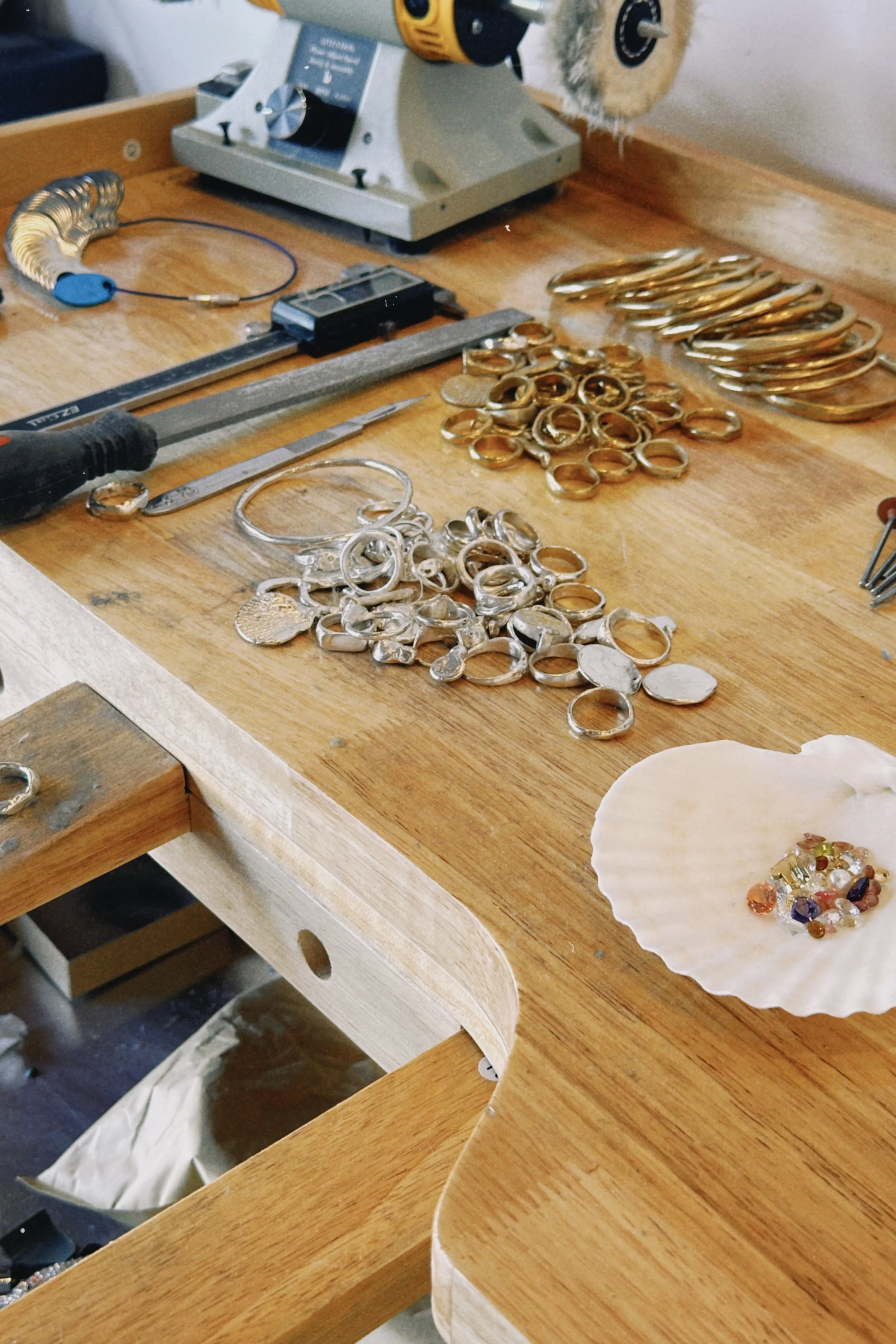 A wooden workbench with jewelry-making tools and various jewelry pieces, including rings, bracelets, and decorative stones.