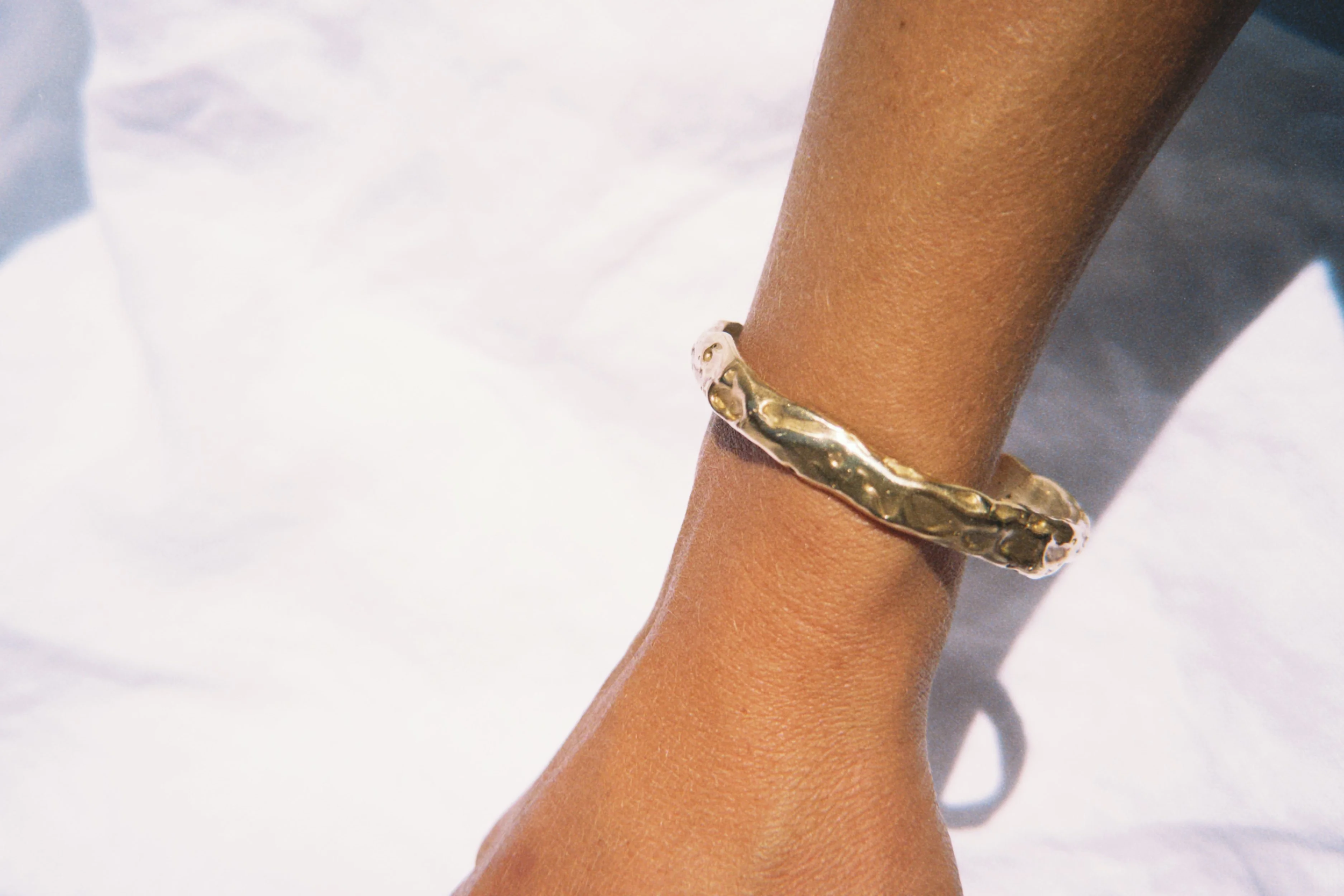 Close-up of a person’s arm with a gold bracelet on the wrist, set against a white background.