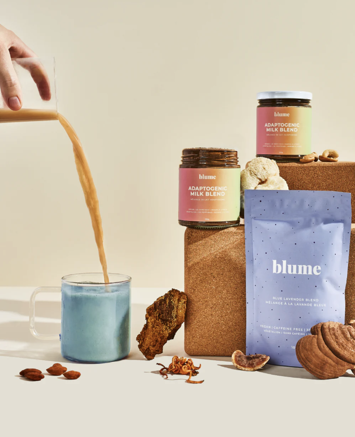 Adaptogenic milk blend containers with a lavender drink being poured, surrounded by various natural ingredients and a package labeled 'blume' against a neutral background.
