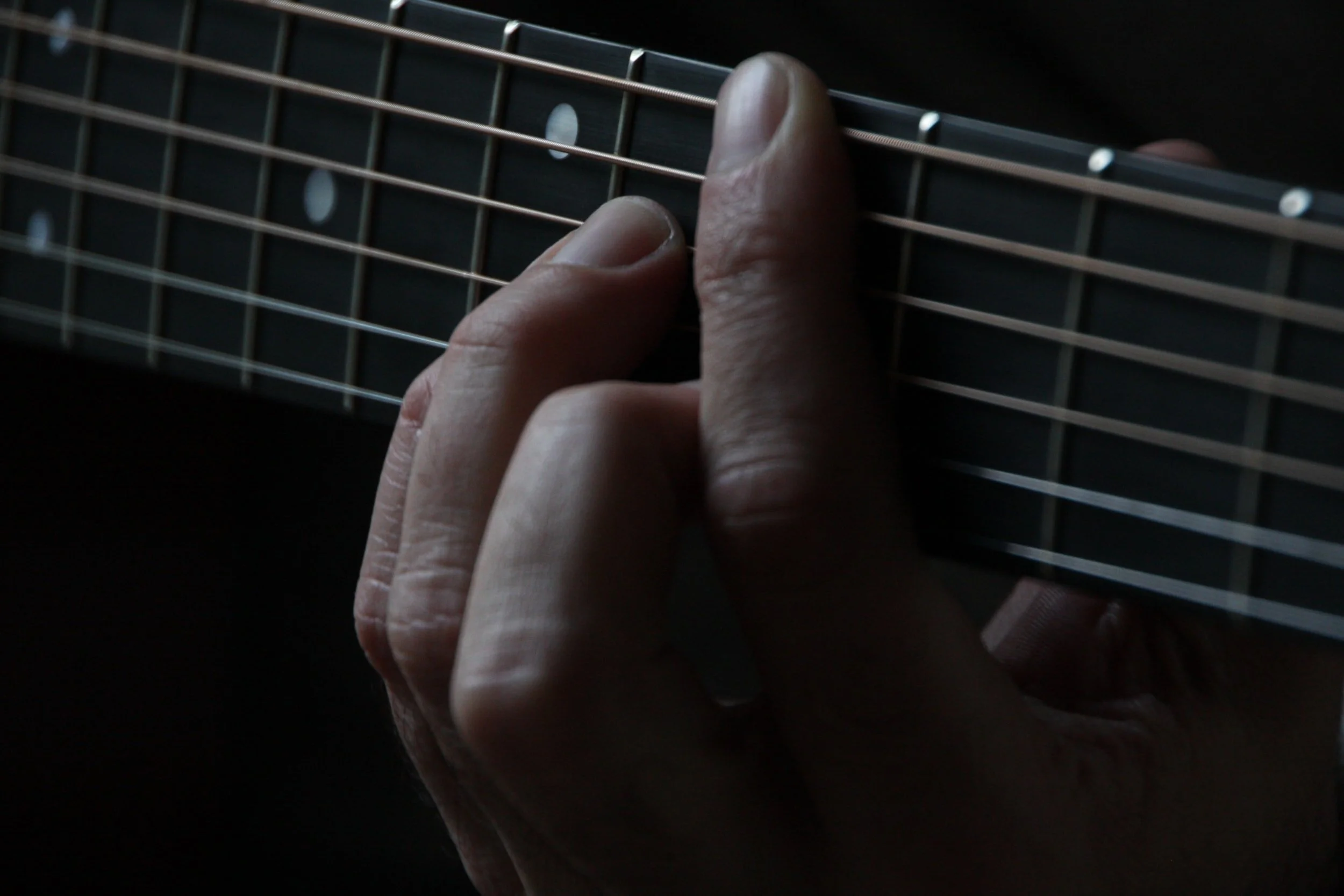 Close-up of a person's hand pressing down on the strings of a guitar fretboard.