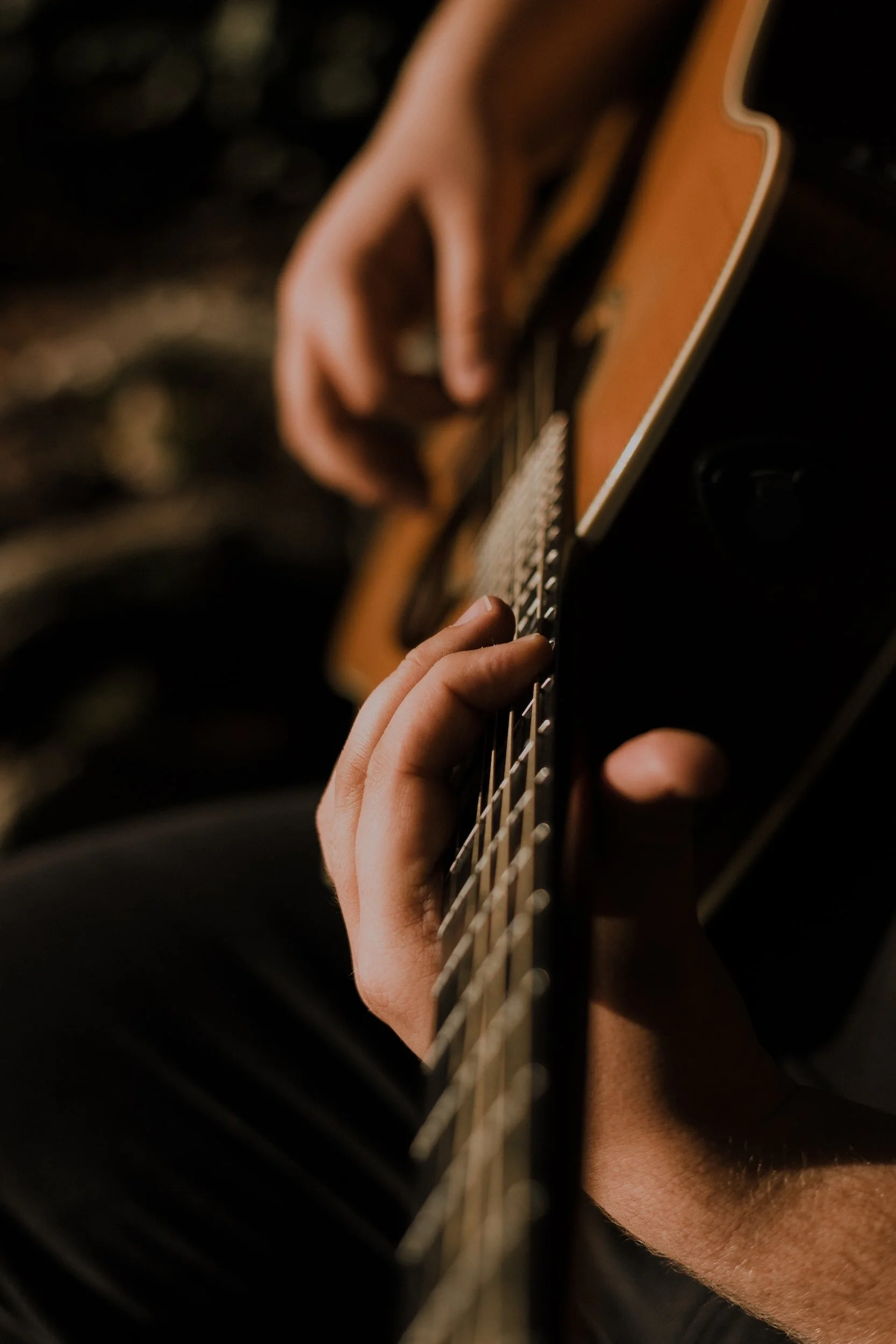 Close-up of a person playing an acoustic guitar, focusing on their hand on the fretboard.
