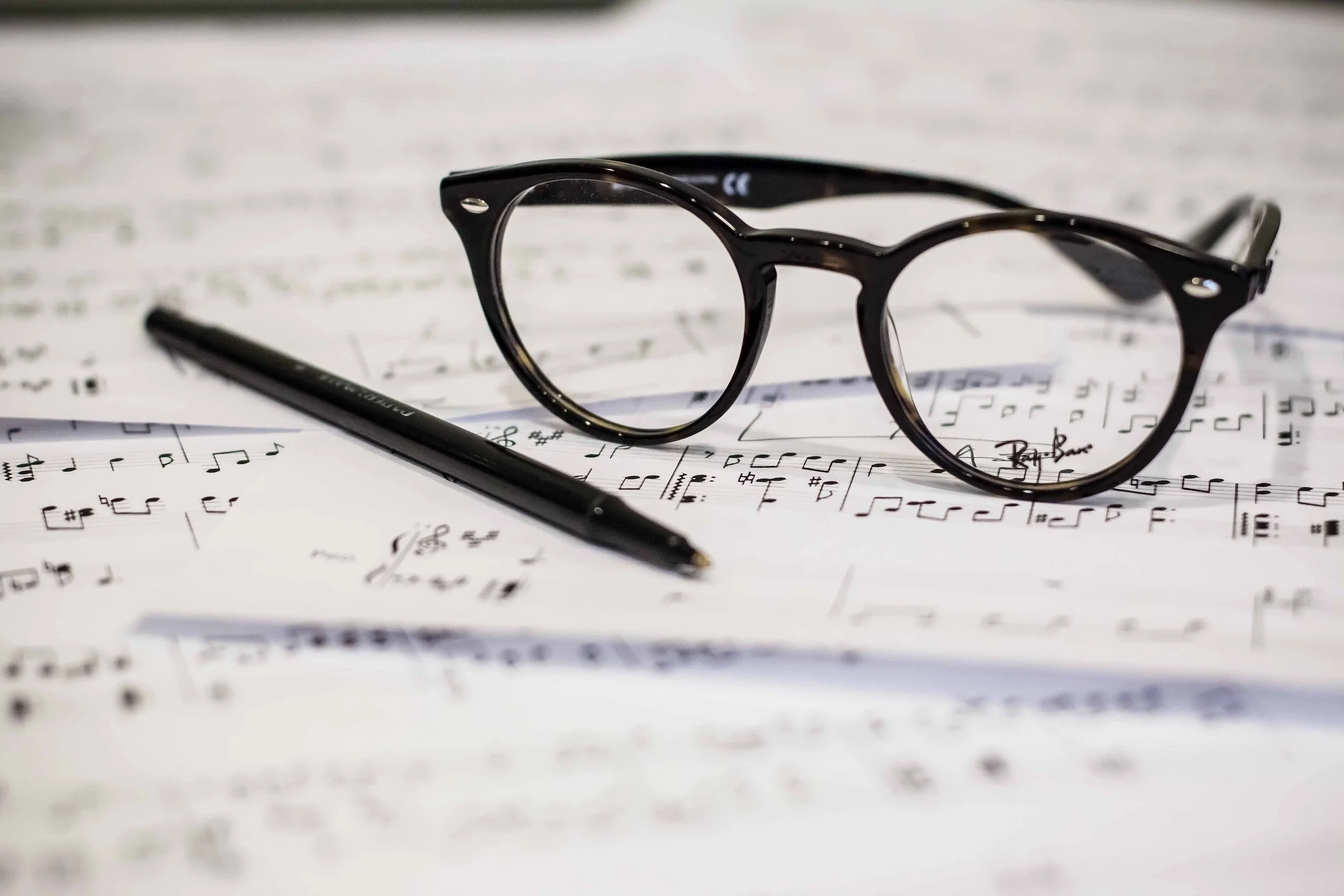 A pair of black eyeglasses and a black pen resting on sheets of sheet music.