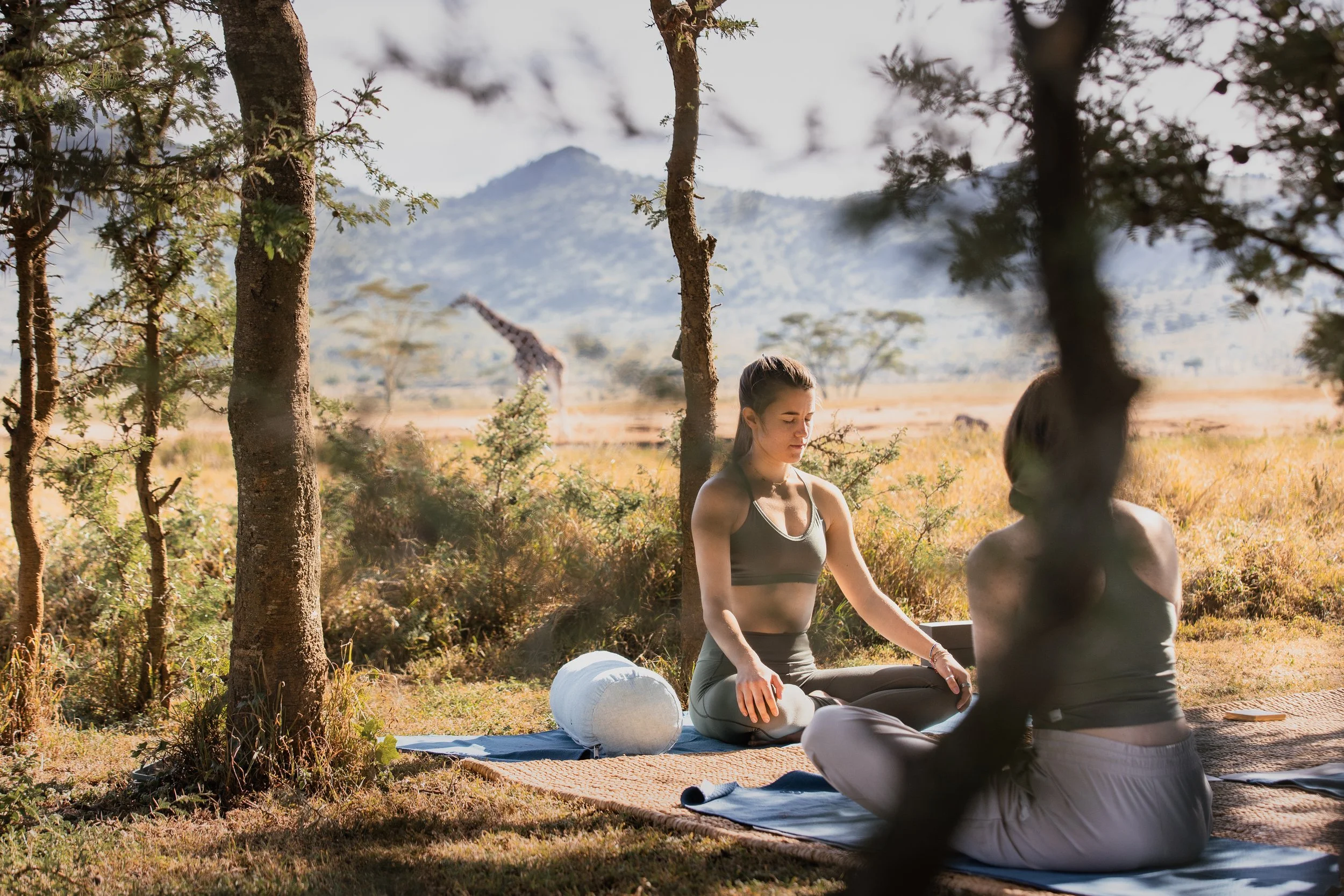Laura and guest practice breathwork and a giraffe is seen in the background