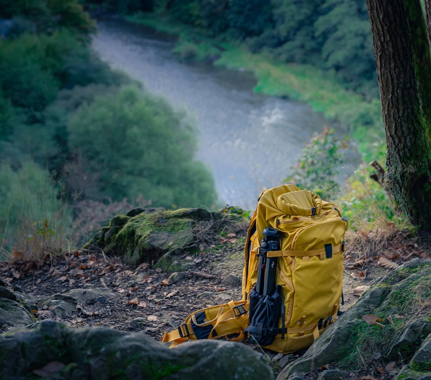 Yellow rucksack with walking poles attached, on some rocks beside a river