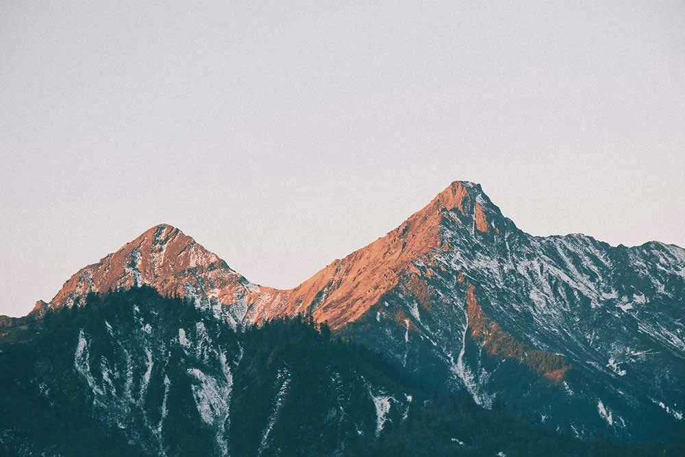 Two rocky mountain peaks, lightly sprinkled with snow, with the sun shining on the highest sections