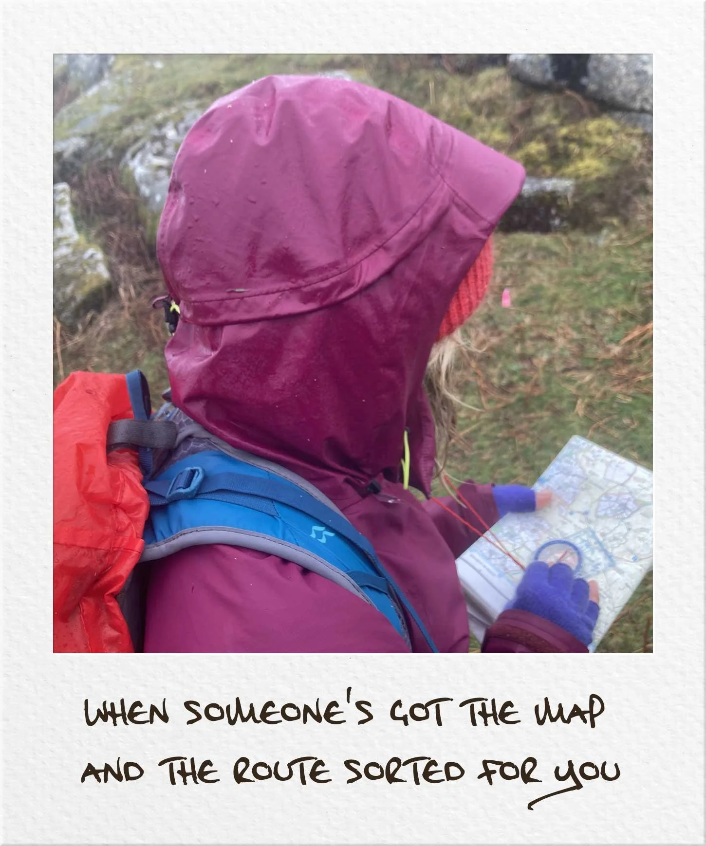 Hiker wearing a purple raincoat, reading a map with a compass in the rain in a polaroid "When someone's got the map and the route sorted for you"